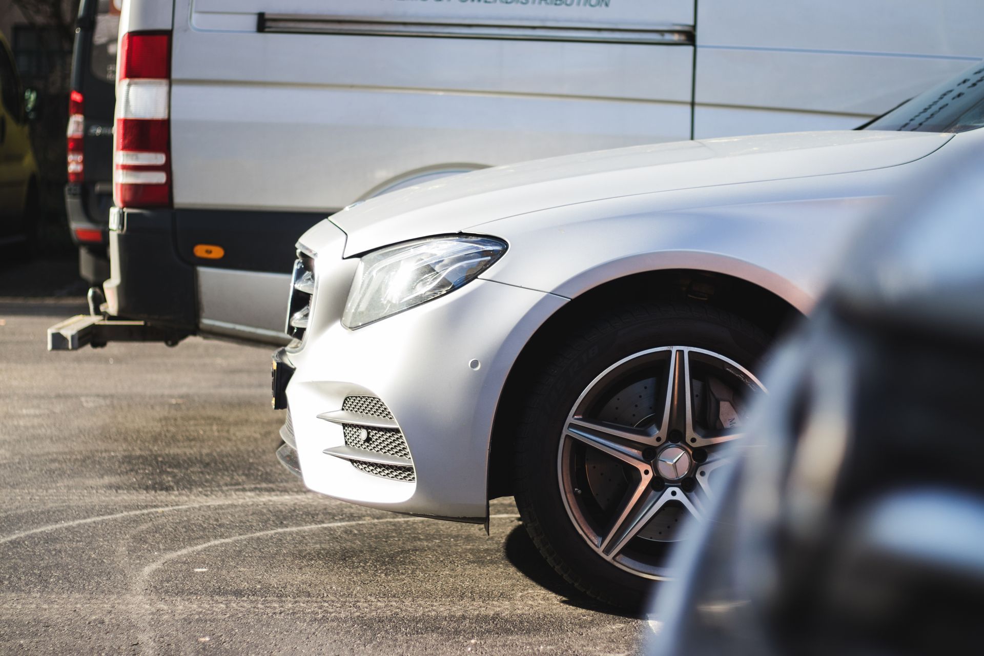 White Mercedes car parked next to a van; the setting appears to be a parking lot.