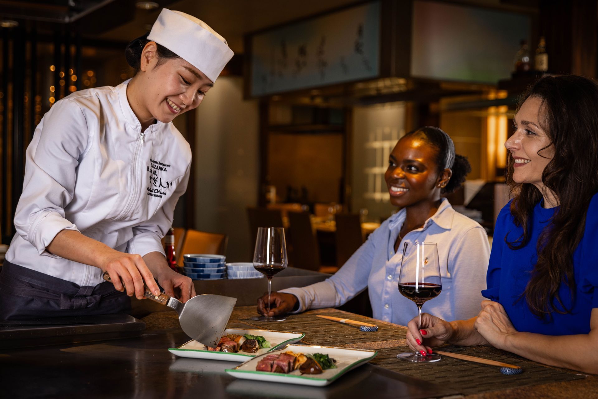 Chef preparing food for two guests at a teppanyaki grill.