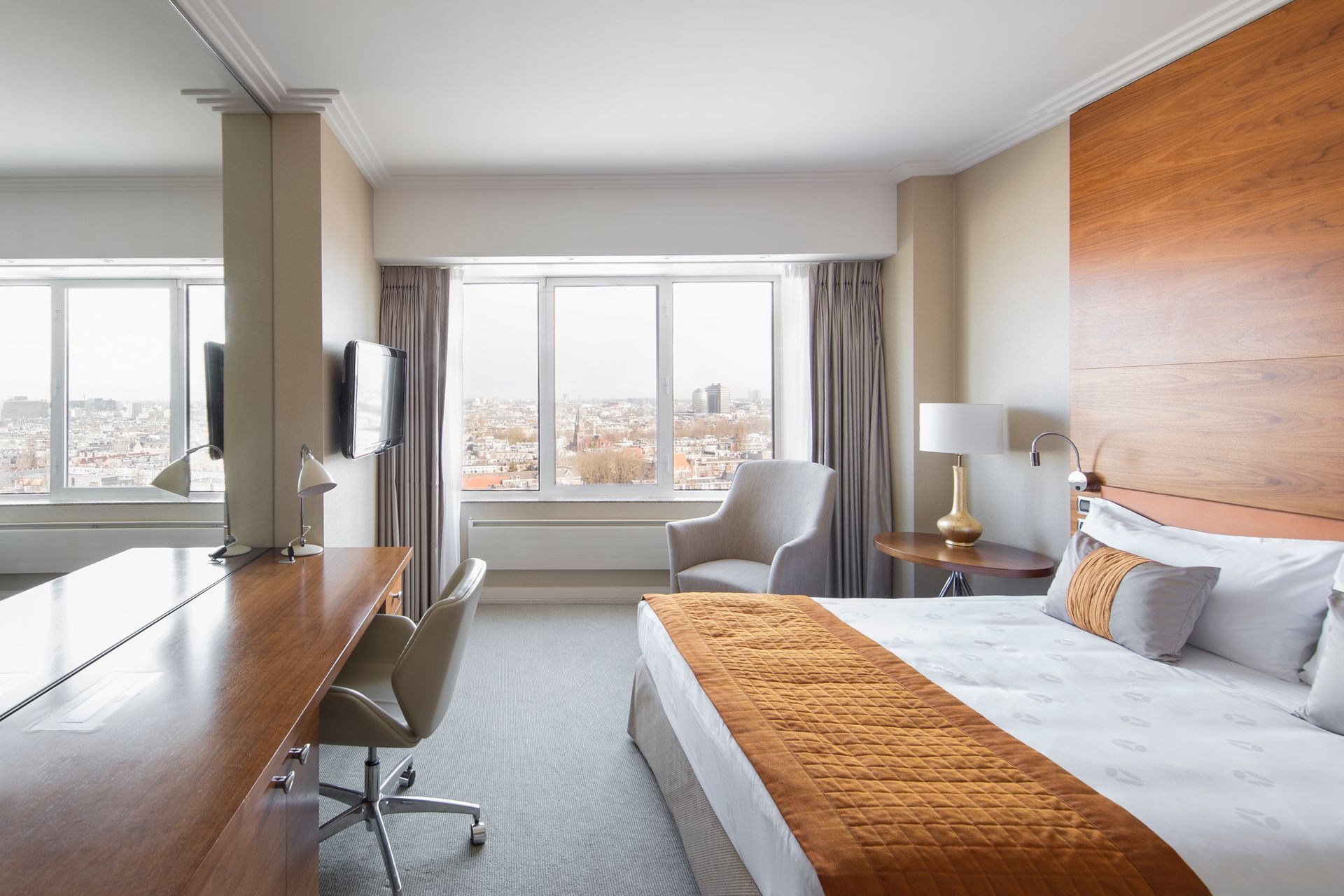 Hotel room with a bed, desk, chair, and large window overlooking a city.