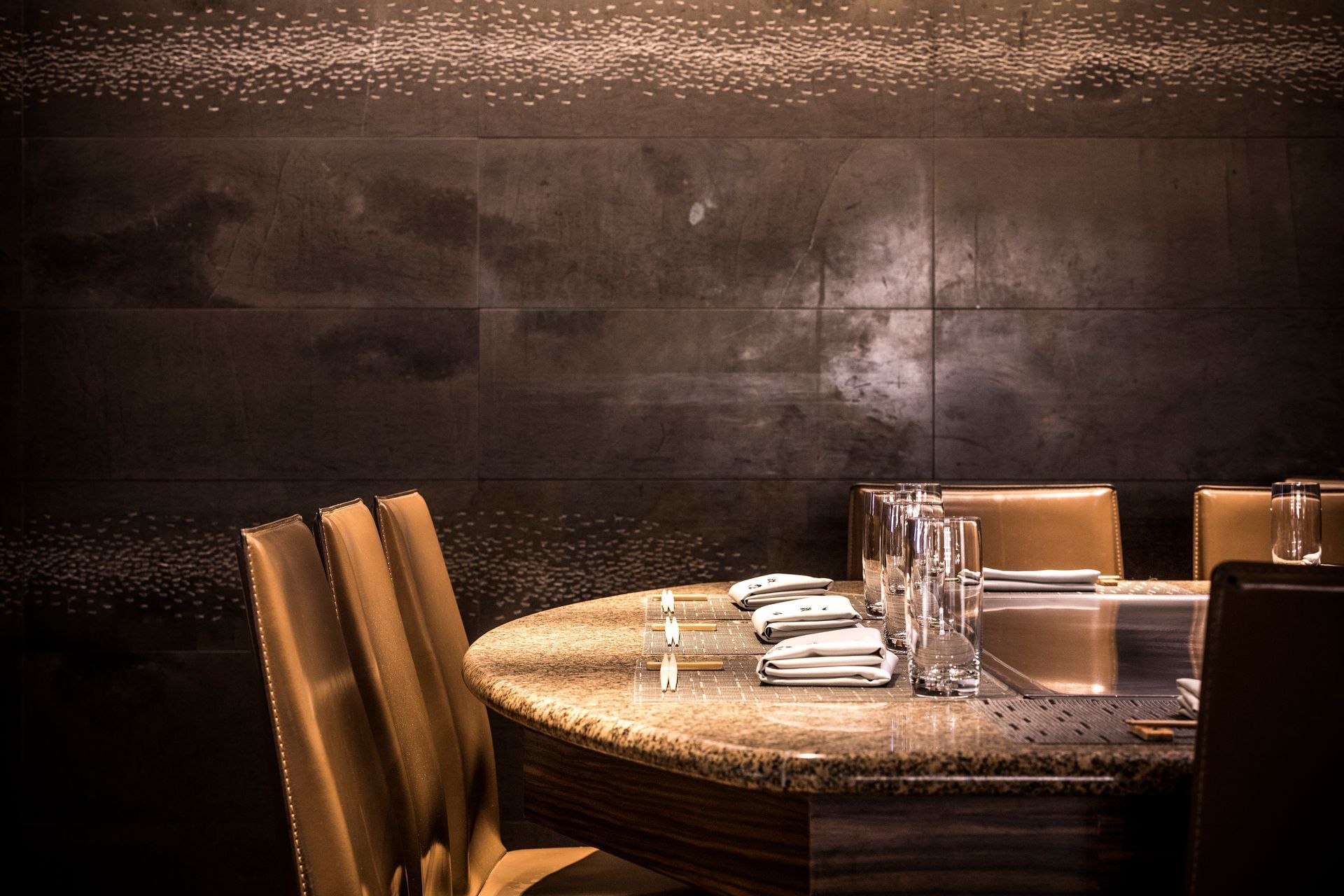 Round table set for a meal, with brown leather chairs, and dark mottled walls.