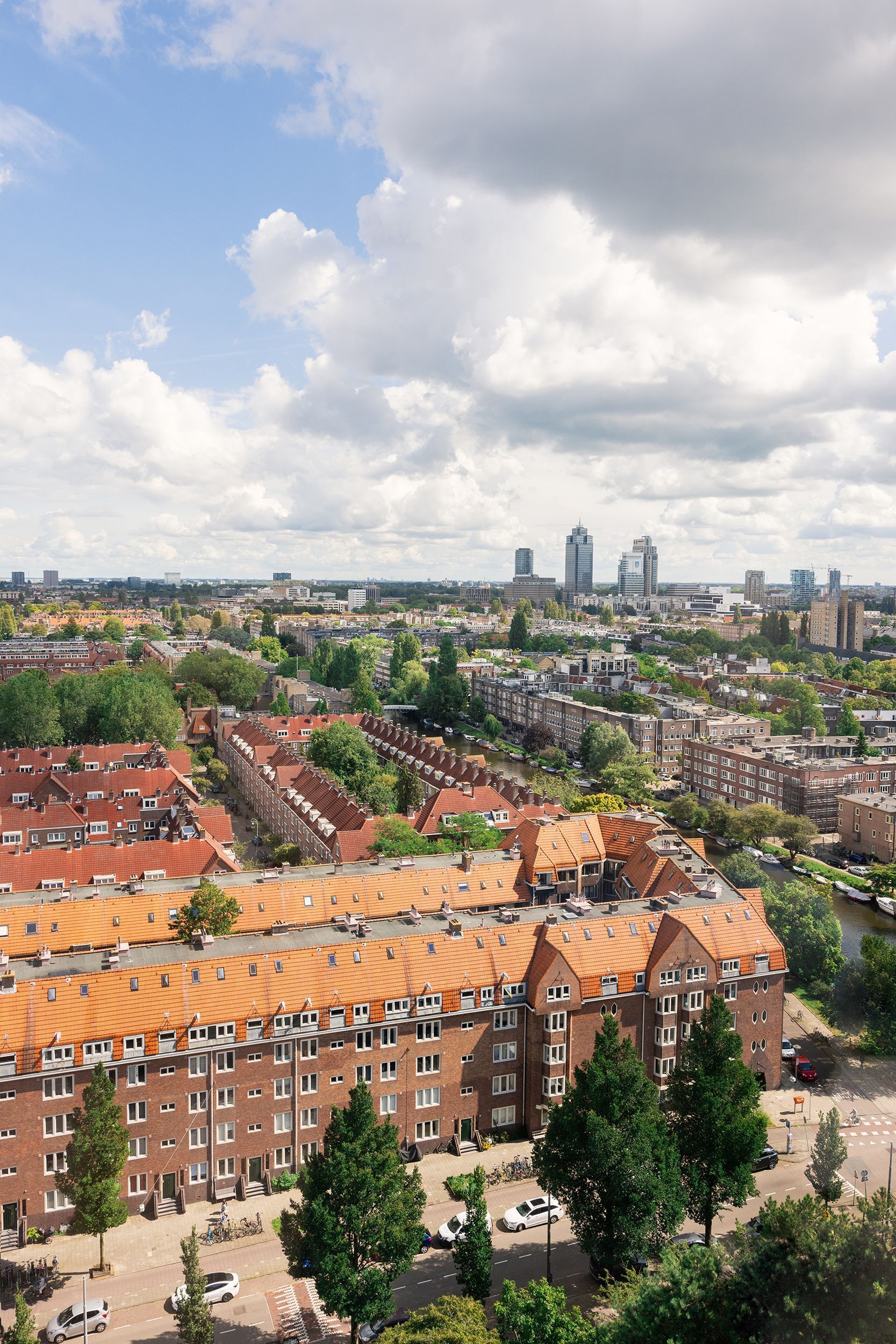 Cityscape view with rows of brick buildings with orange roofs, trees, and cloudy sky.