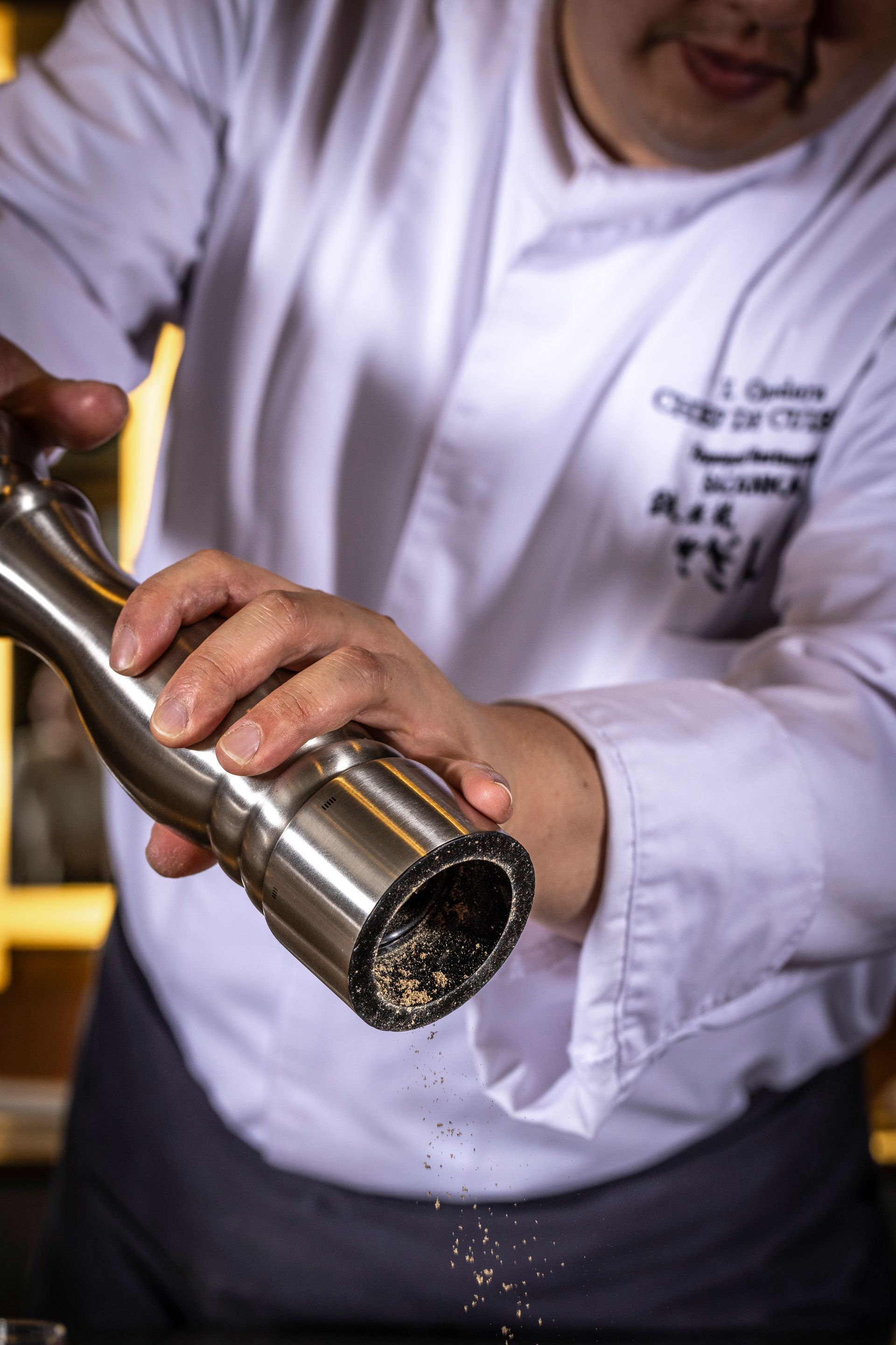 Chef grinding pepper, white coat, close-up.