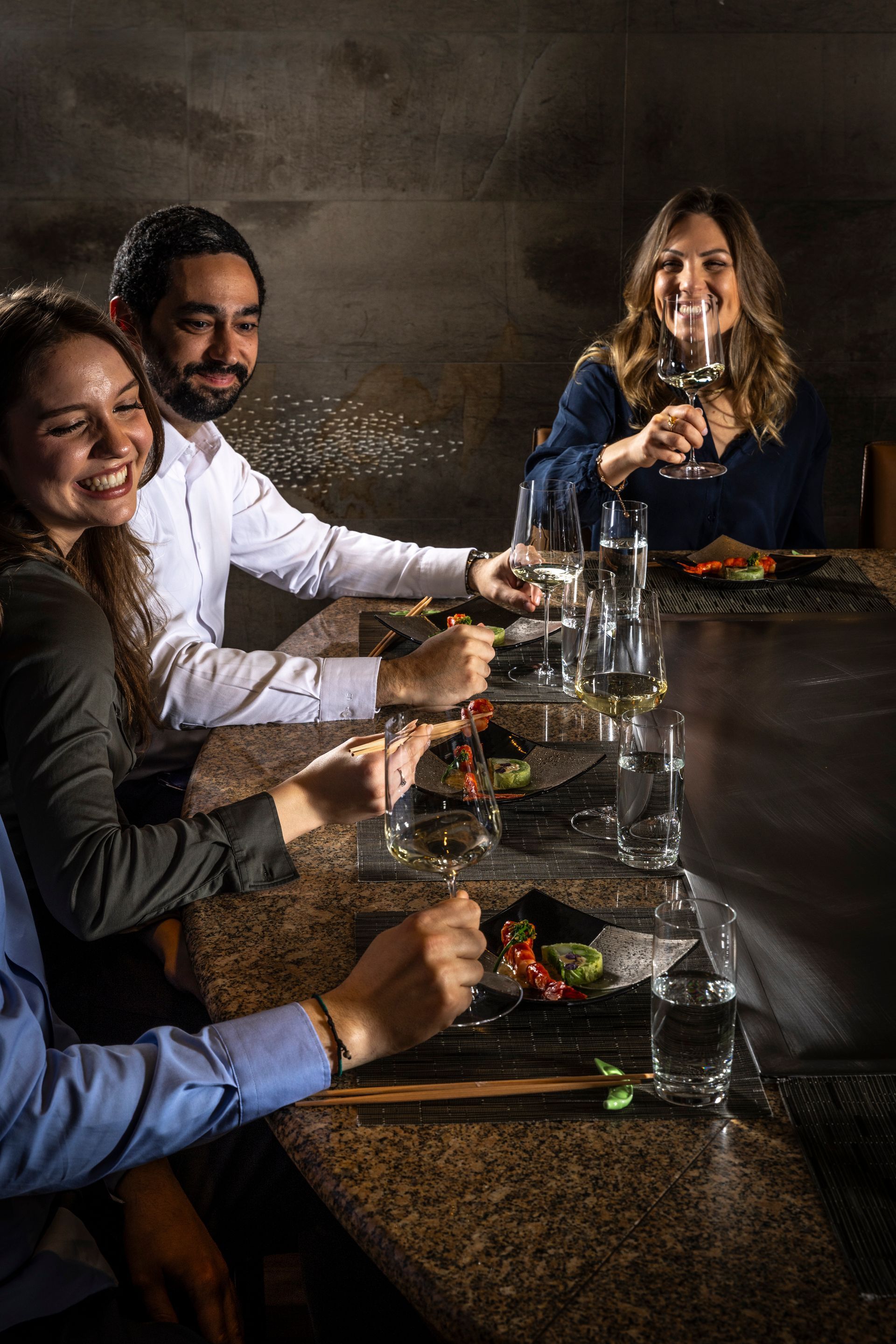 People enjoying wine at a restaurant table. They are smiling, with food and glasses visible.
