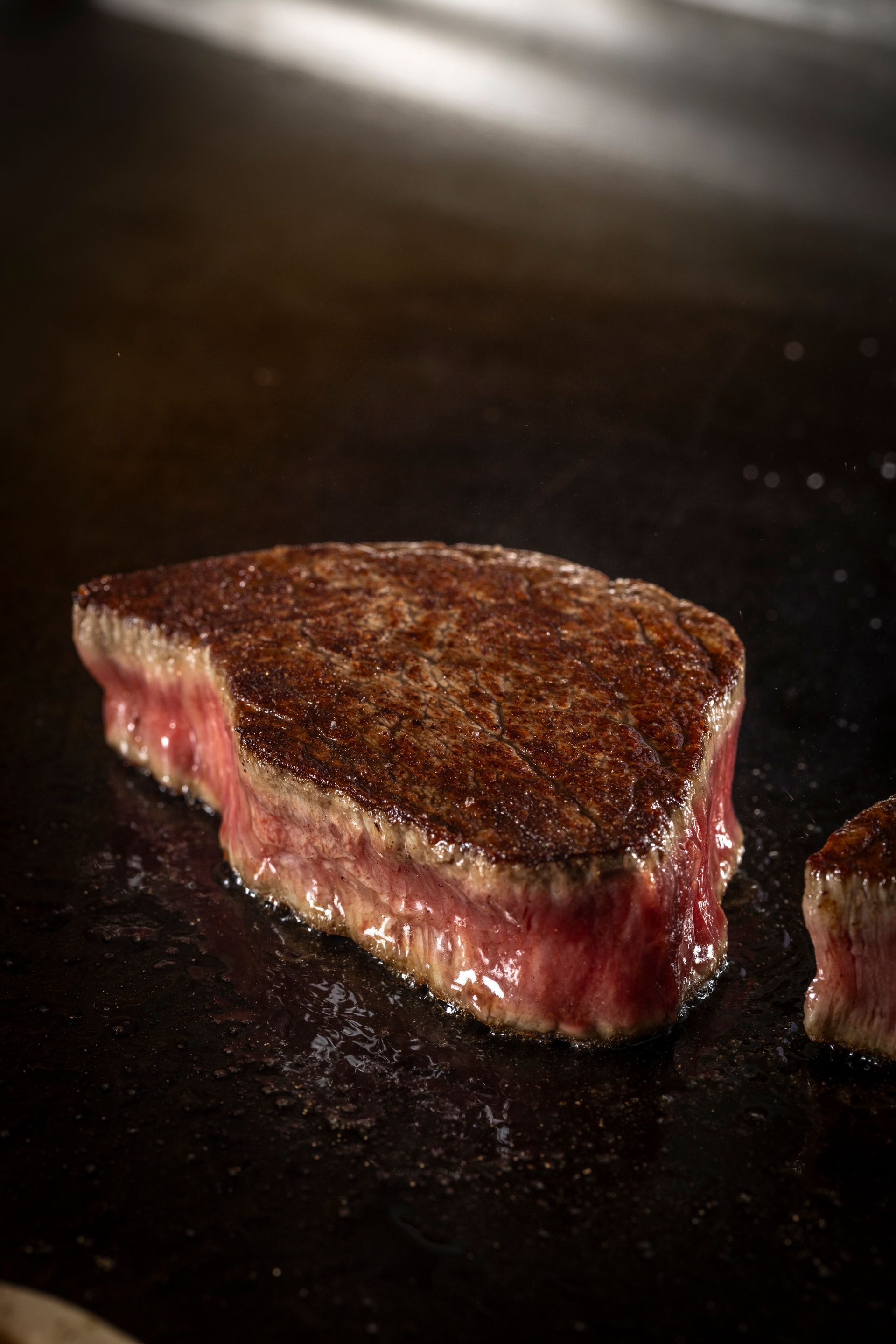 Seared steak on a hot surface, displaying a browned crust and pink interior.