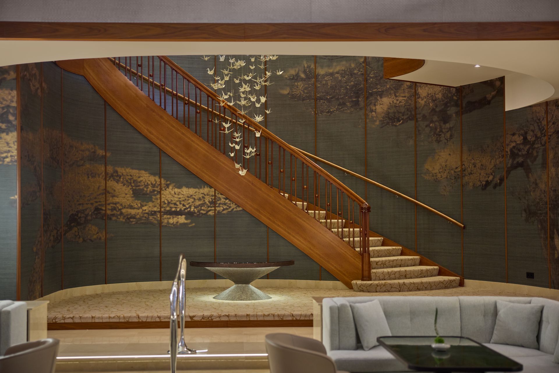 Wooden staircase in a modern, luxury interior with a tiled accent wall and seating area.