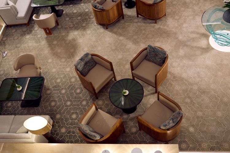 Overhead view of a hotel lobby with seating areas, including chairs and round tables on a patterned carpet.