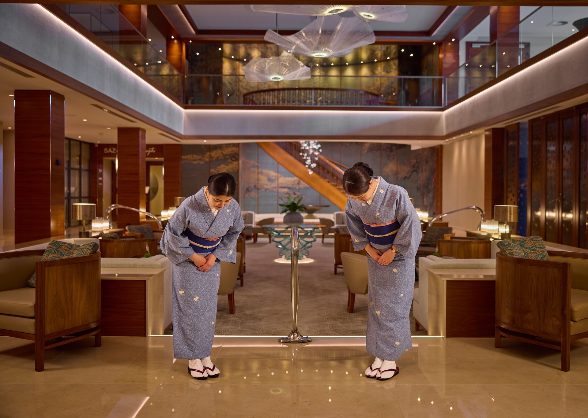 Two women in kimonos bowing inside a hotel lobby.