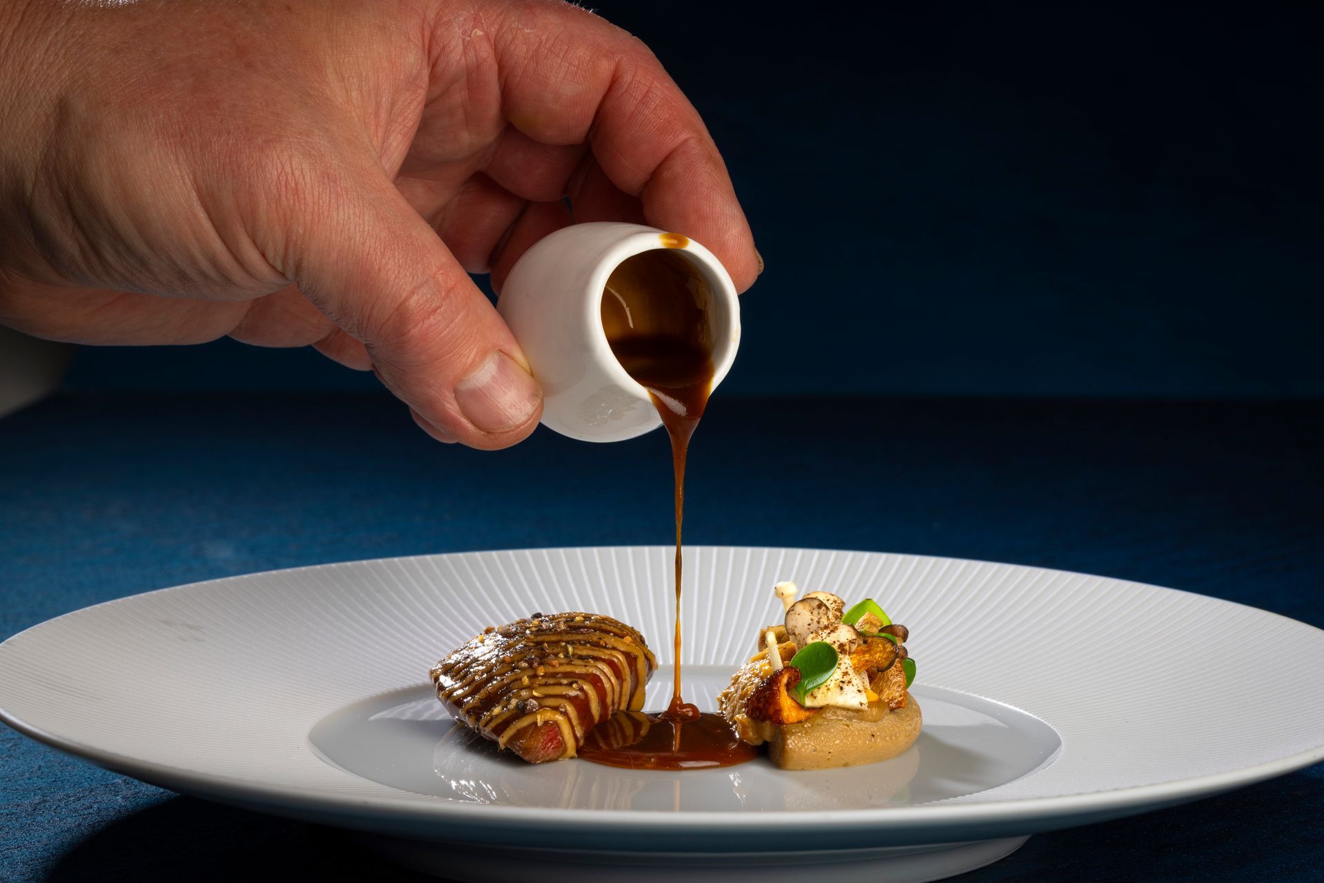 Een ober serveert een kleurrijk voorgerecht op een wit bord aan een lachende gast aan een restauranttafel.