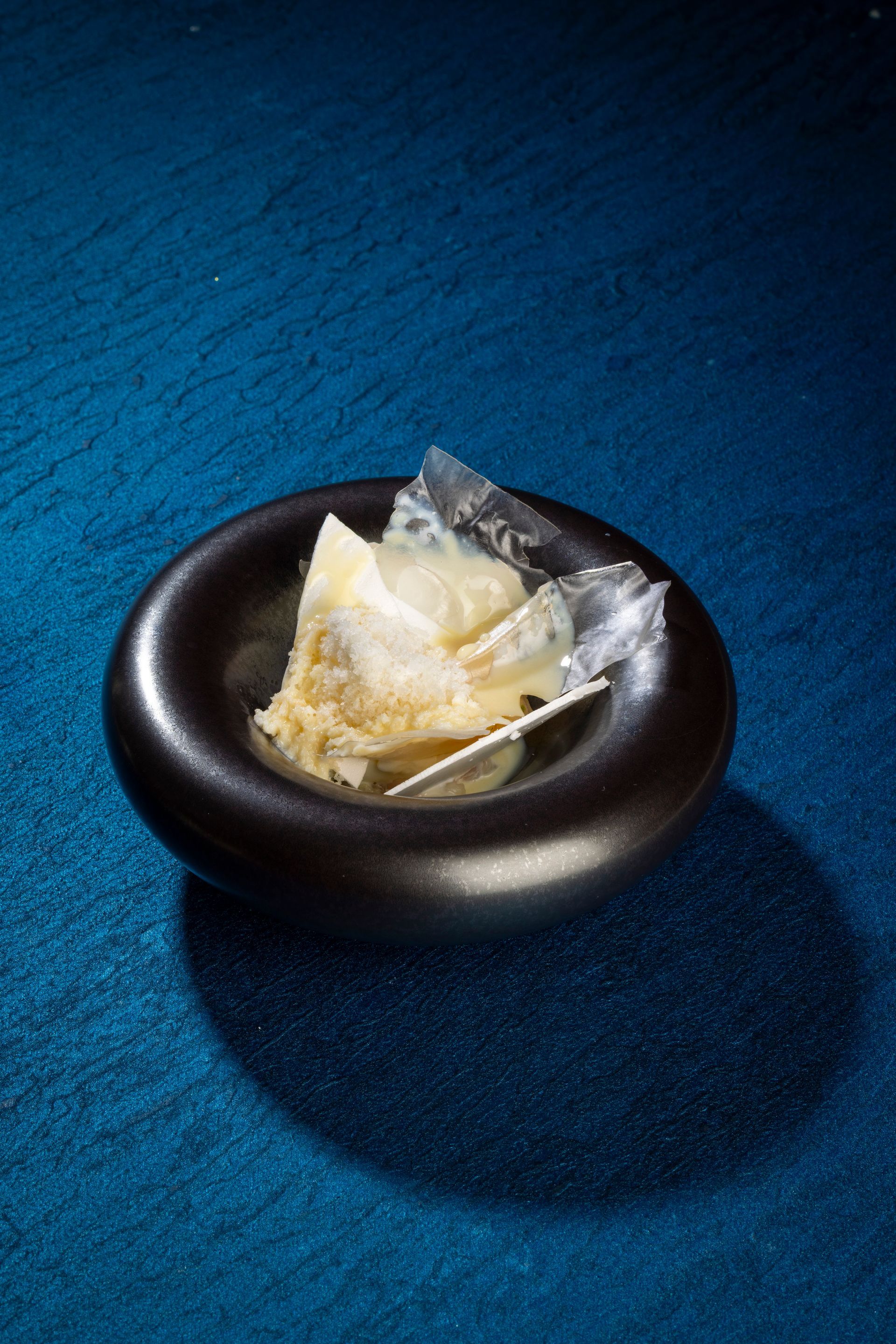 Een ober in een blauw pak giet saus over een gerecht aan een restauranttafel met uitzicht op de stad.