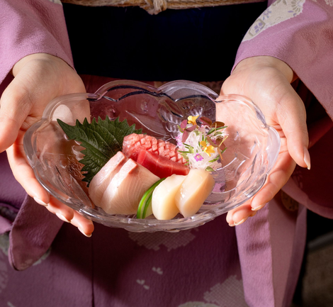 Woman setting a table in a Japanese-style restaurant with wooden decor and large windows.