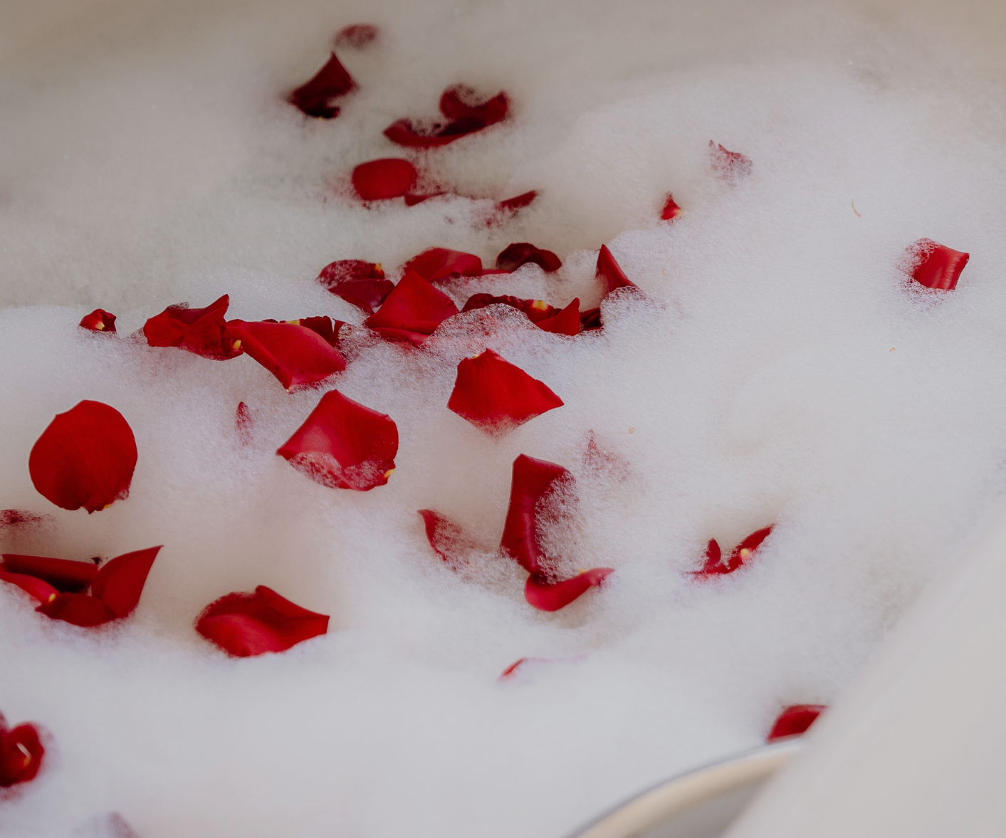 White bath with red rose petals and thick white foam.