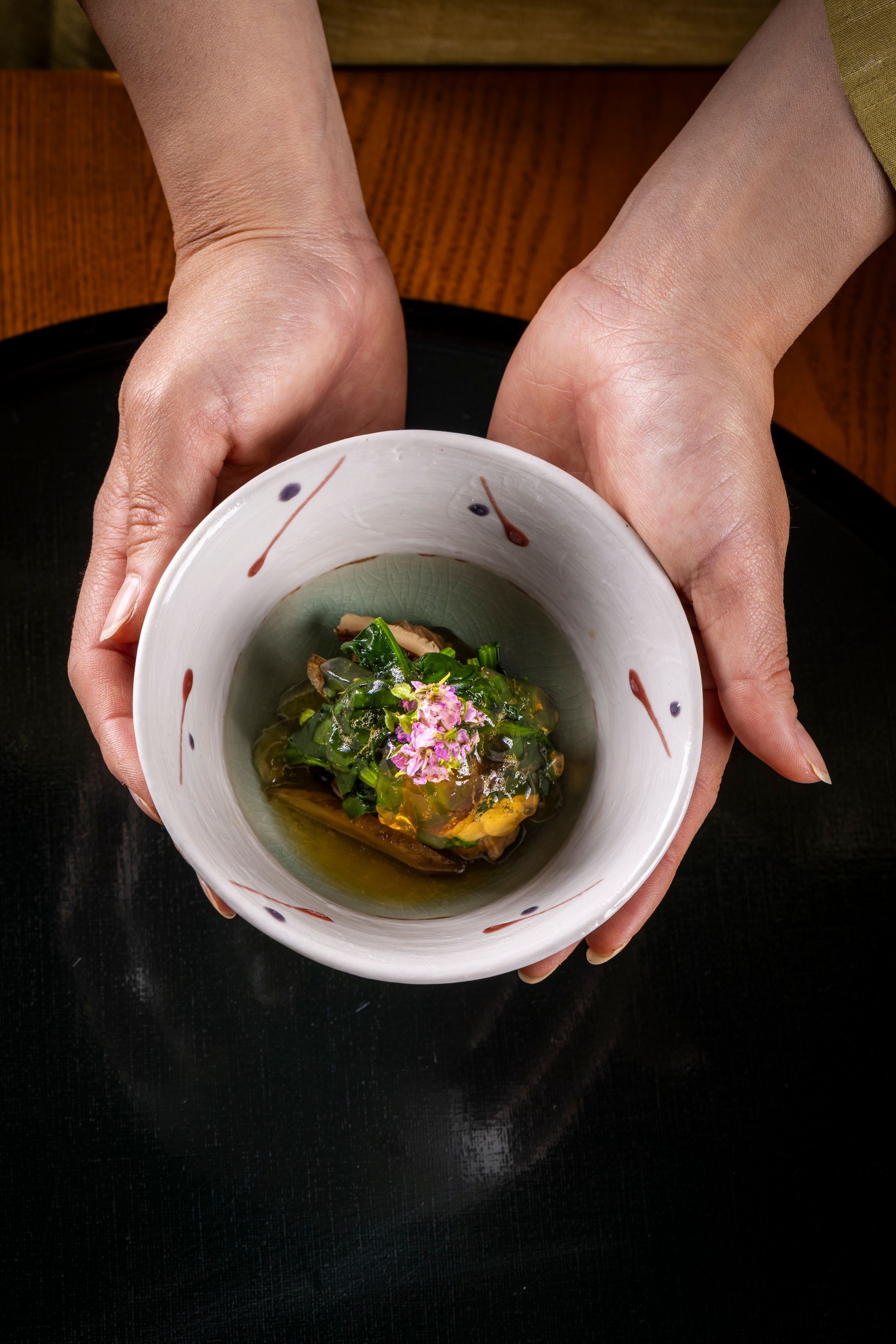 Woman setting a table in a Japanese-style restaurant with wooden decor and large windows.