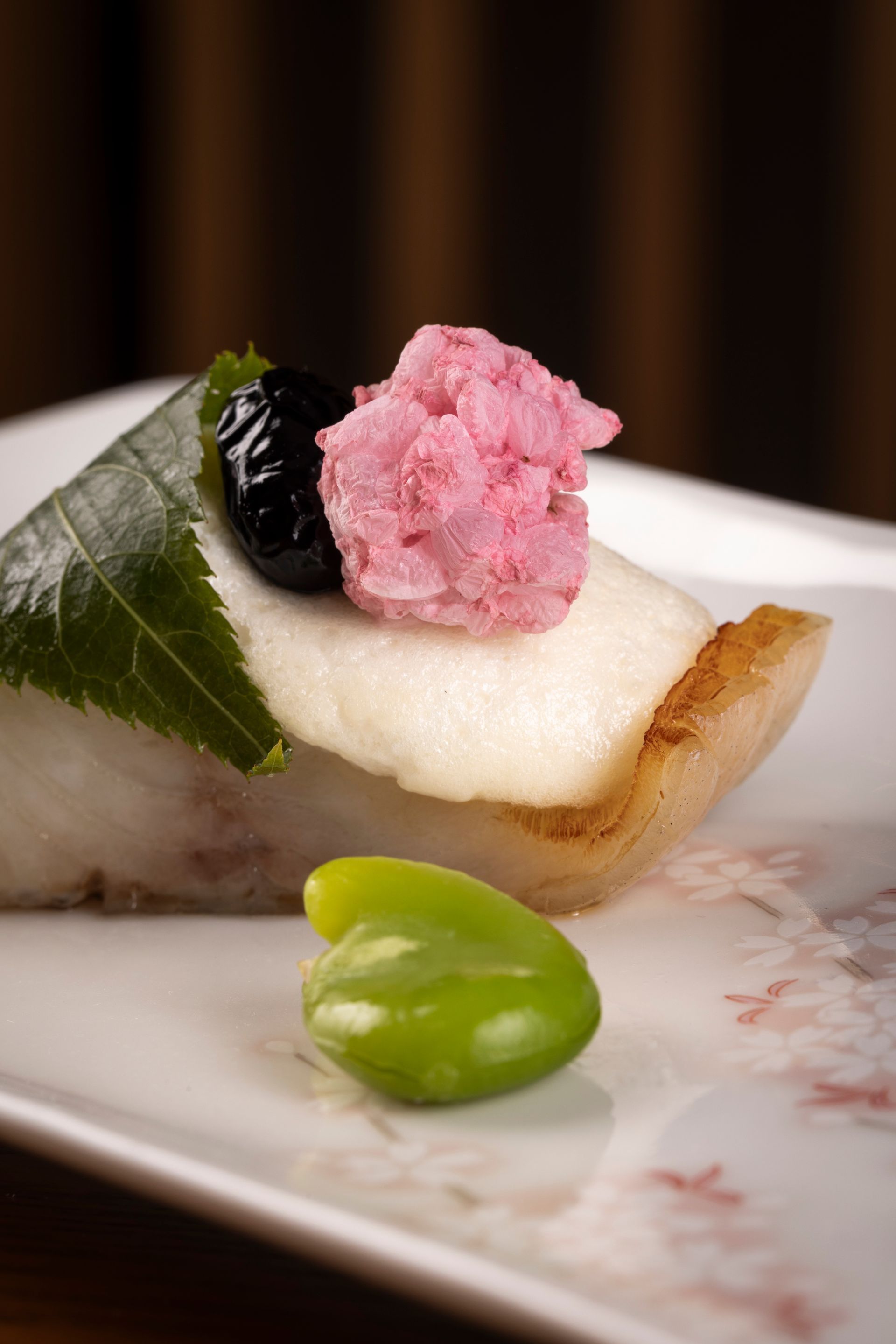 Japanese mochi cake with toppings, decorated with a leaf, beans, and pink flower petals.