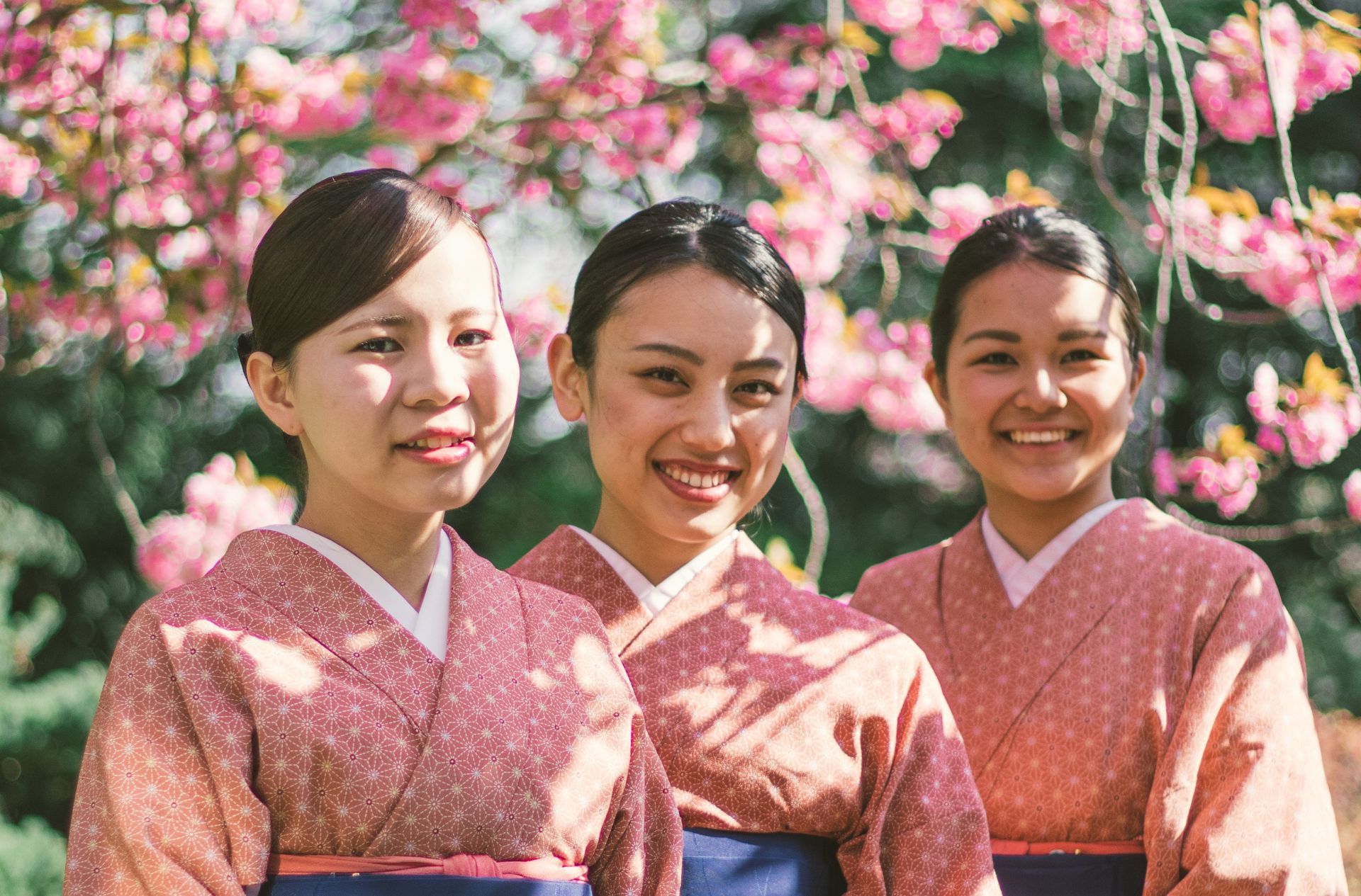 Two women in yukata stand in front of a green, leafy background.
