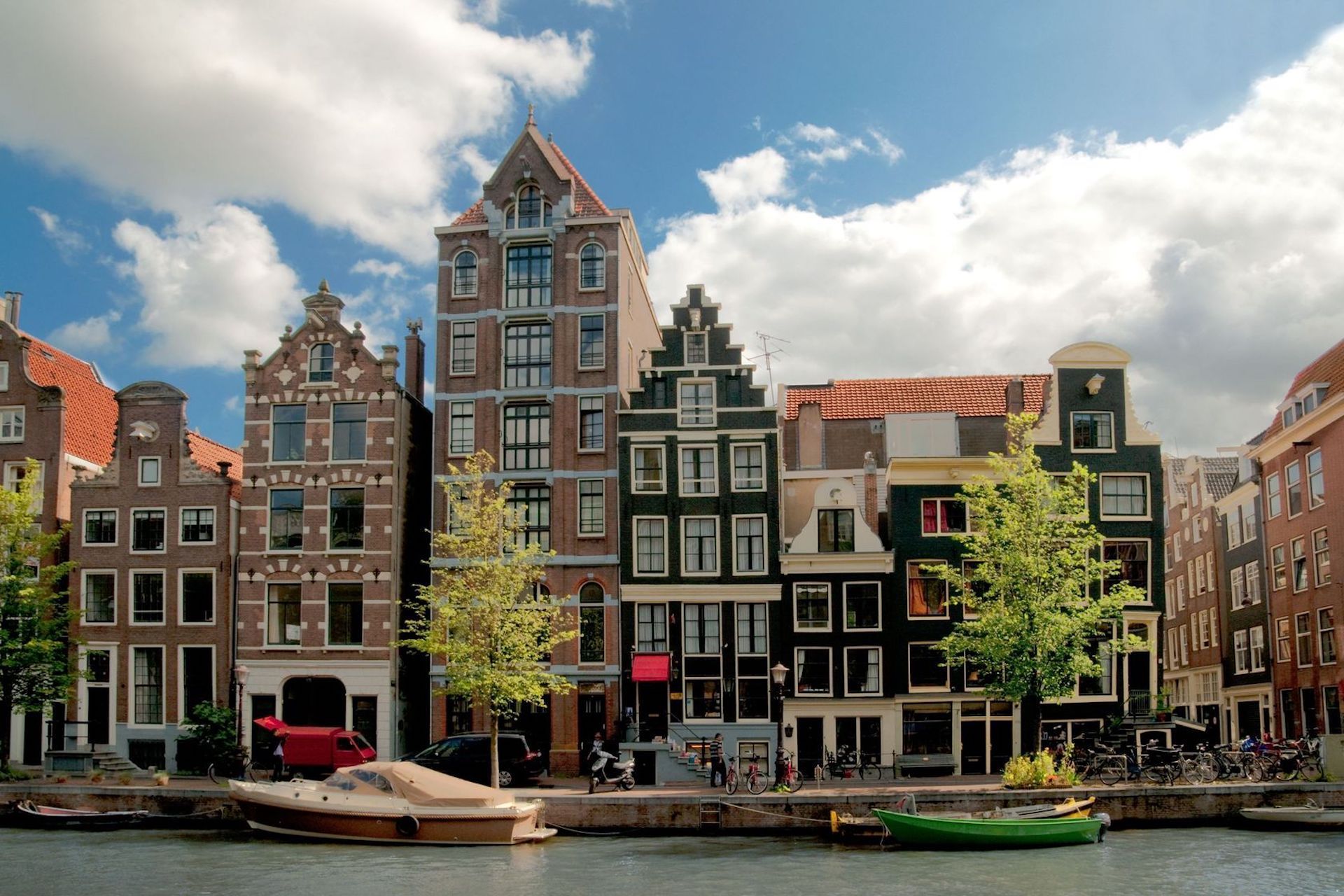 Canal-side buildings in Amsterdam, Netherlands. Tall, narrow buildings with gabled facades. Boat floats on water.