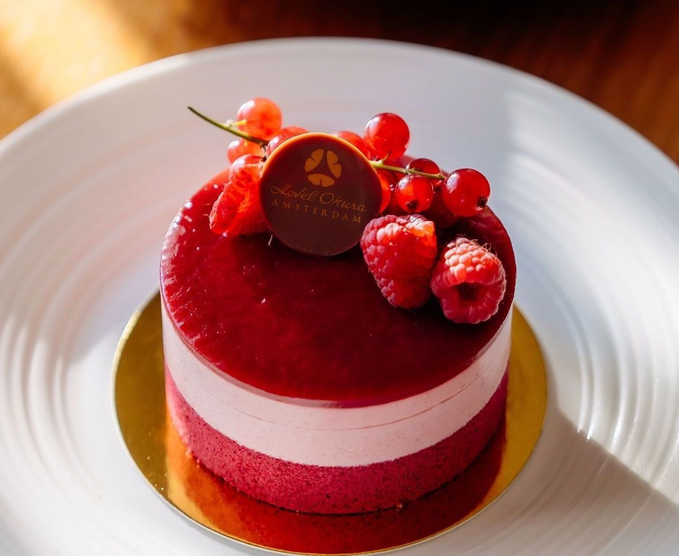 Round red dessert with a berry topping, sitting on a gold base, and a white plate.