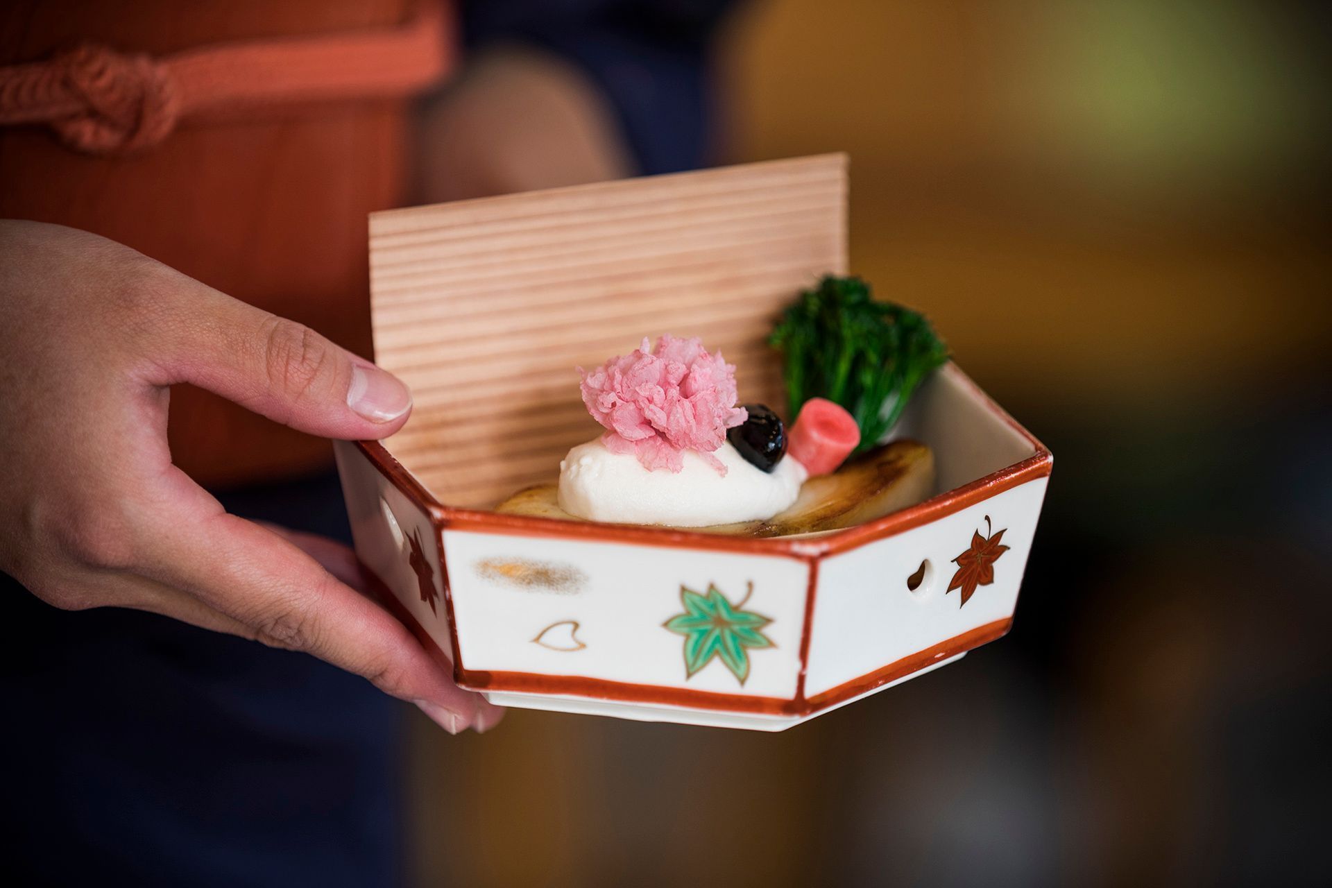 Person holding a decorative wooden bento box with food shaped like a pig.