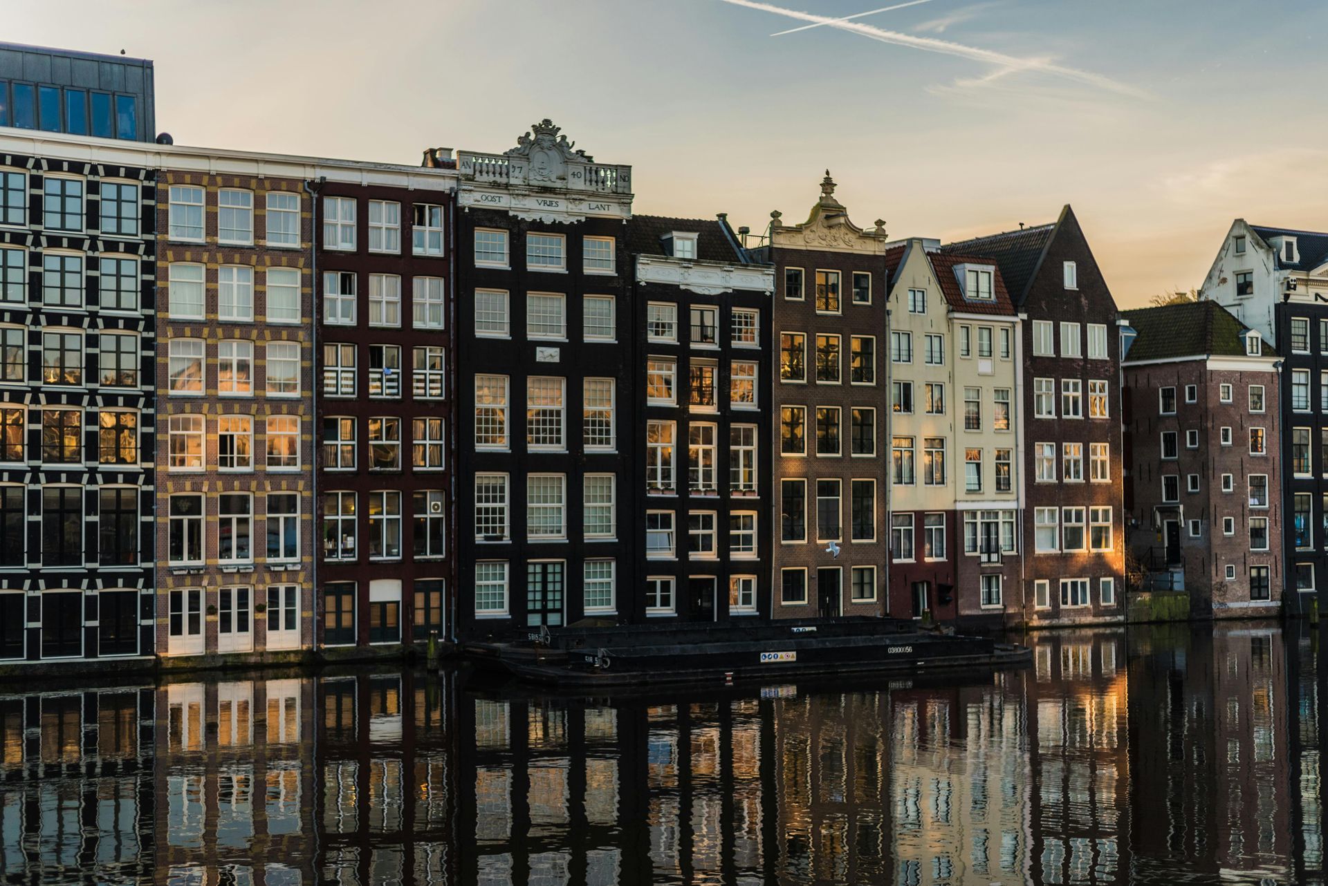 Canal houses in Amsterdam reflected in the water; brown, beige, and white facades.