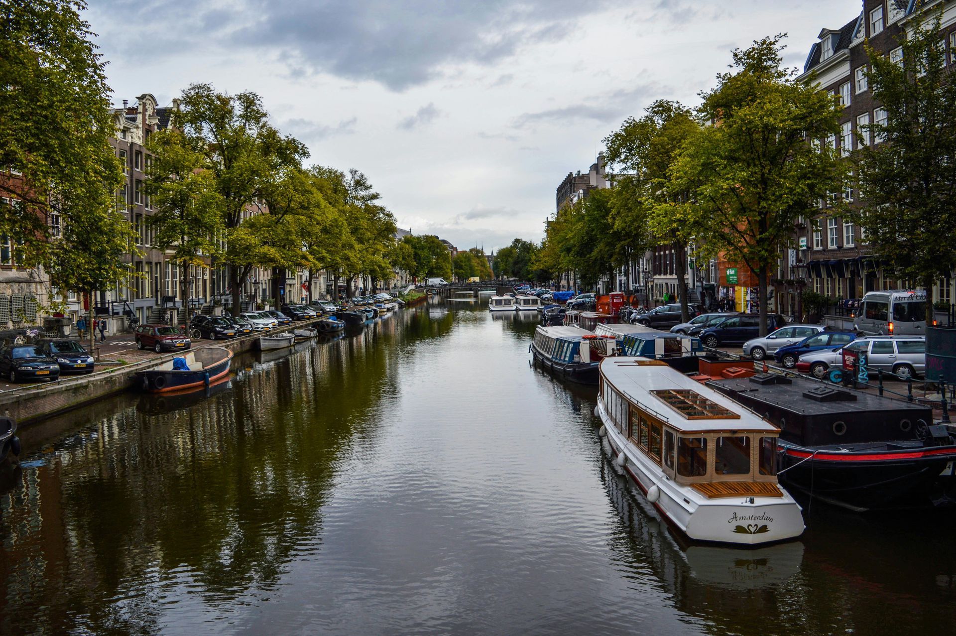 Kanaal in Amsterdam, omzoomd met boten en gebouwen, onder een bewolkte lucht.