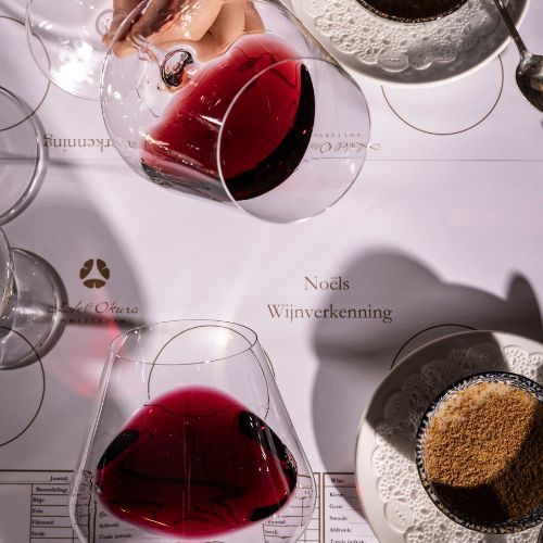 Overhead view of wine glasses with red wine on a table, plus a hand pouring, and small plates with brown sugar.