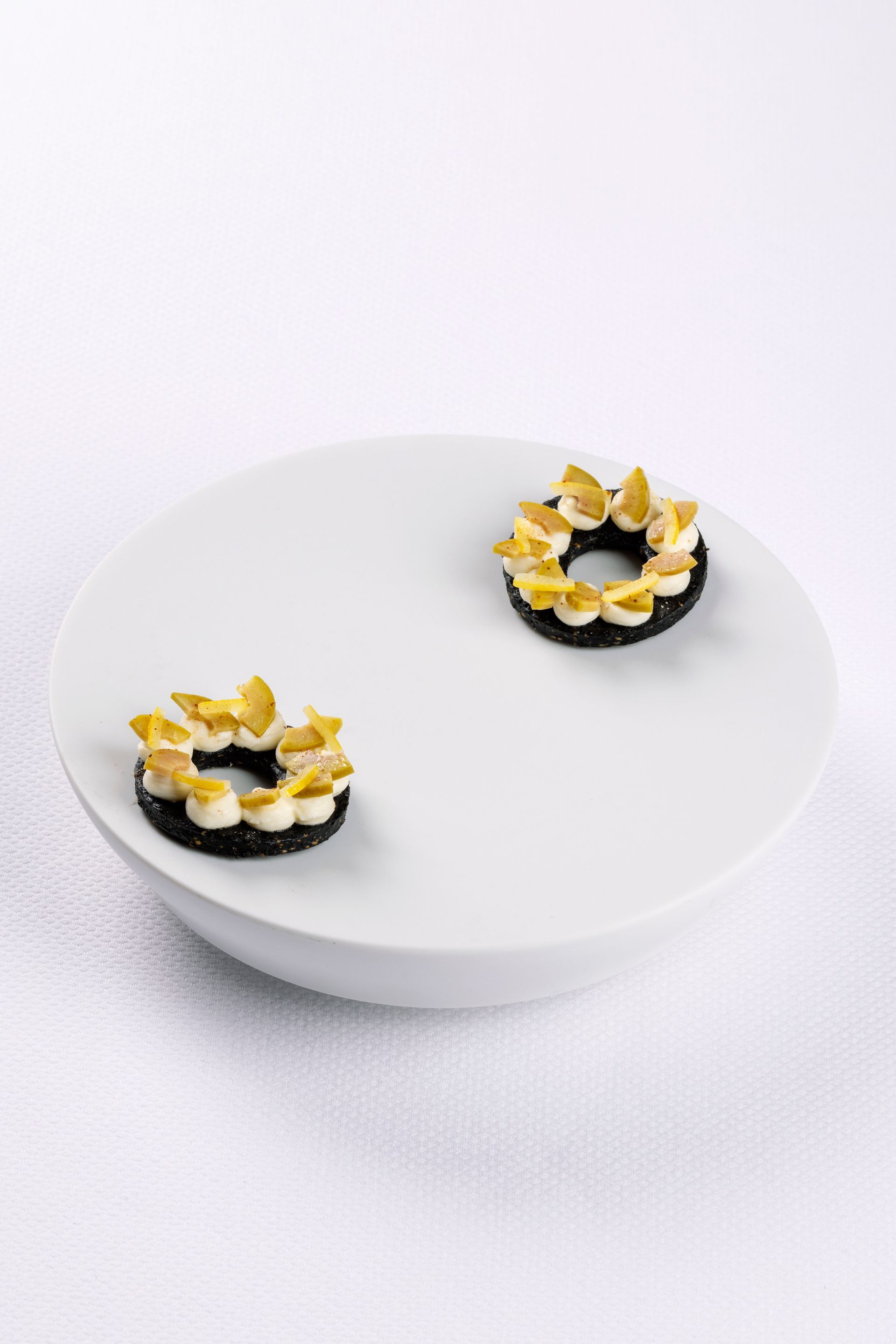 Two small, ring-shaped desserts with yellow and white toppings on a white plate.