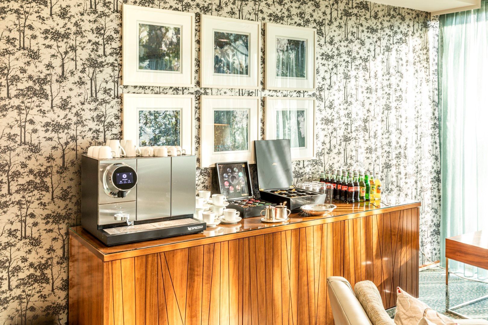 Coffee station on wooden cabinet against wallpaper with framed art.