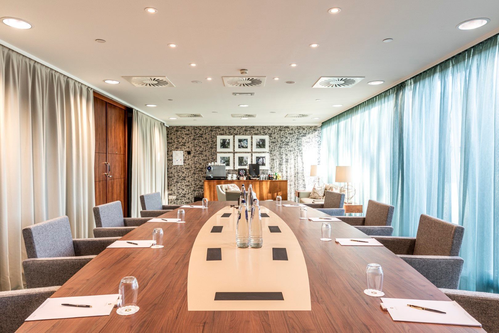 Conference room with a long wooden table, chairs, and curtains.
