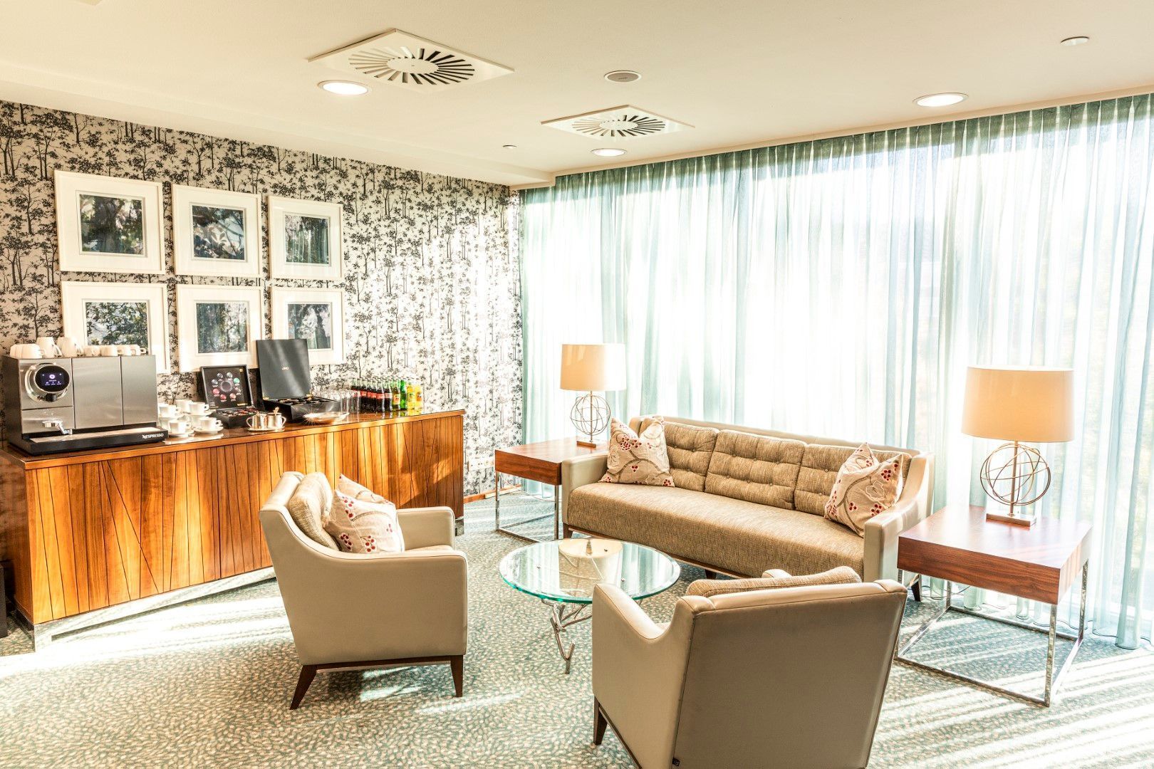 A bright living room with seating, side tables, and a wooden cabinet with framed photos.