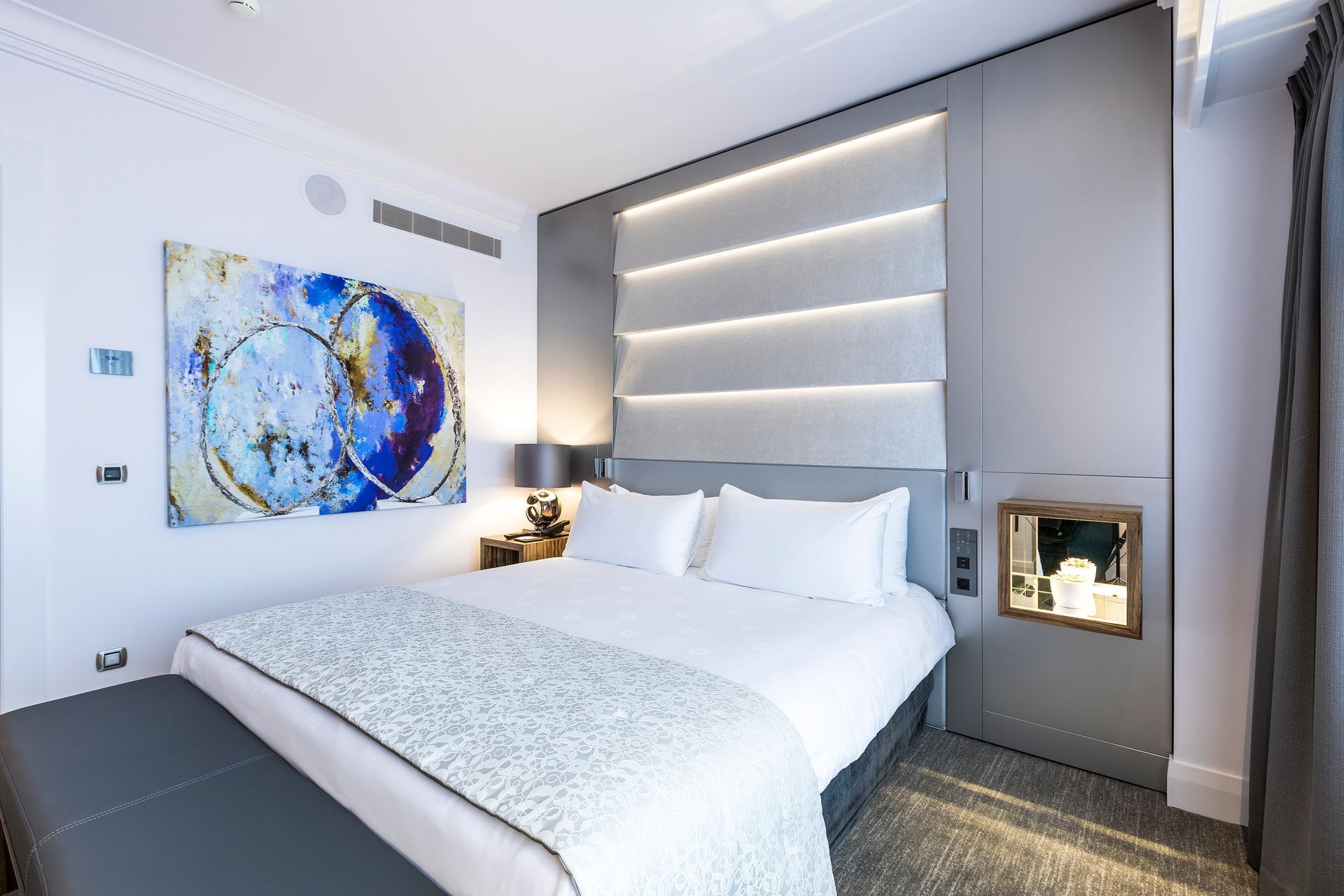 Hotel bedroom with a bed, artwork, and modern wall design.