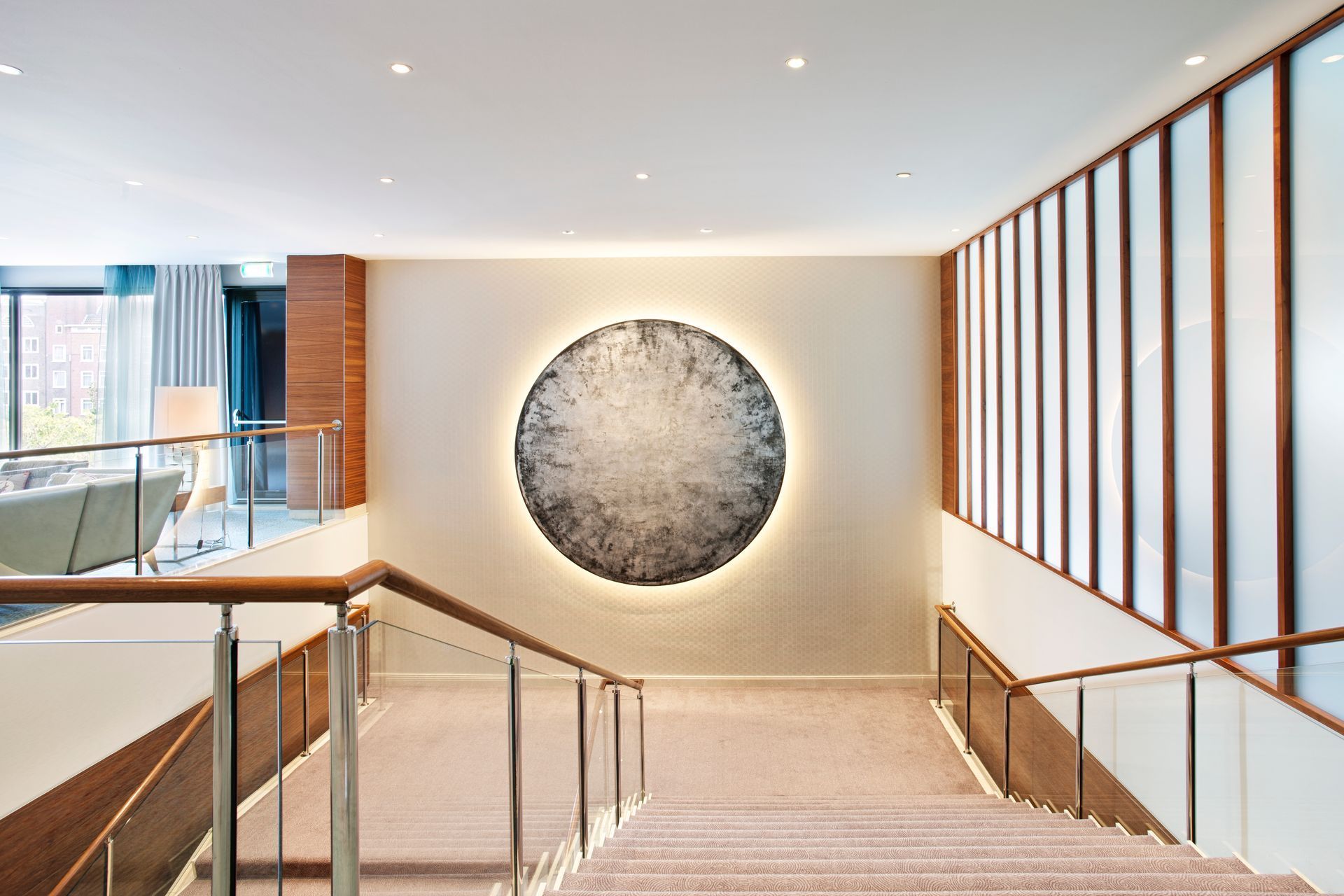 Stairway with wood handrails, a large round illuminated artwork, and frosted glass panels.