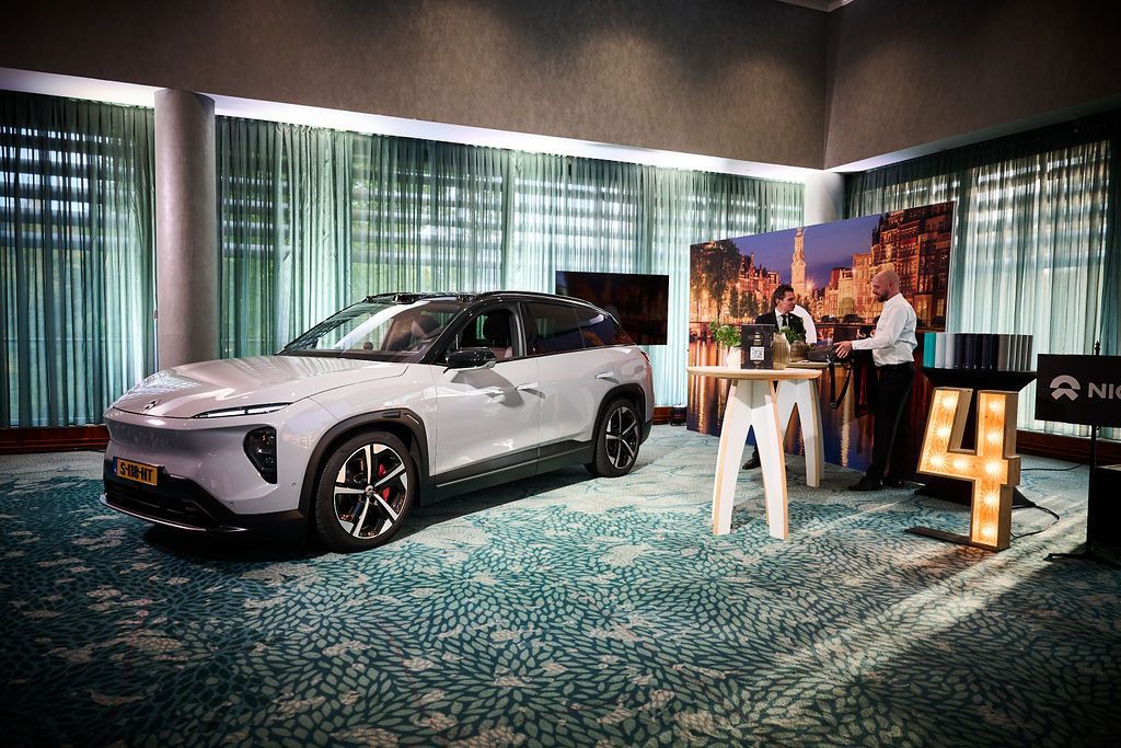 Light grey electric vehicle in a room with a presentation setup. Person standing near a display, 