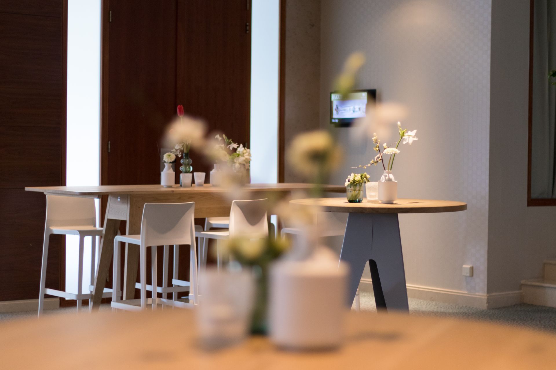 Bar area with tables, chairs, and vases of flowers. A small TV is on the wall.