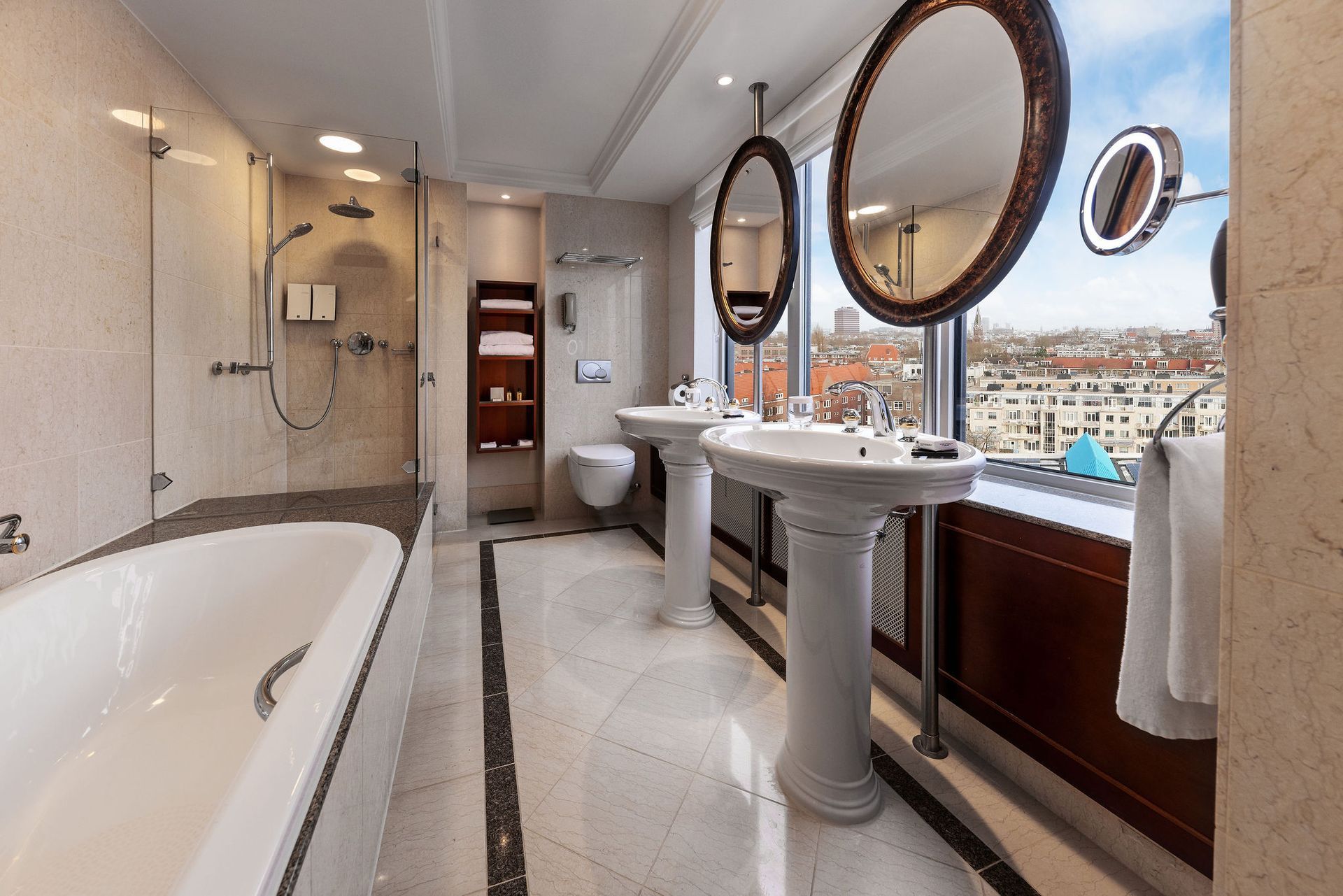 Luxurious hotel bathroom with a soaking tub, dual sinks, and city view.
