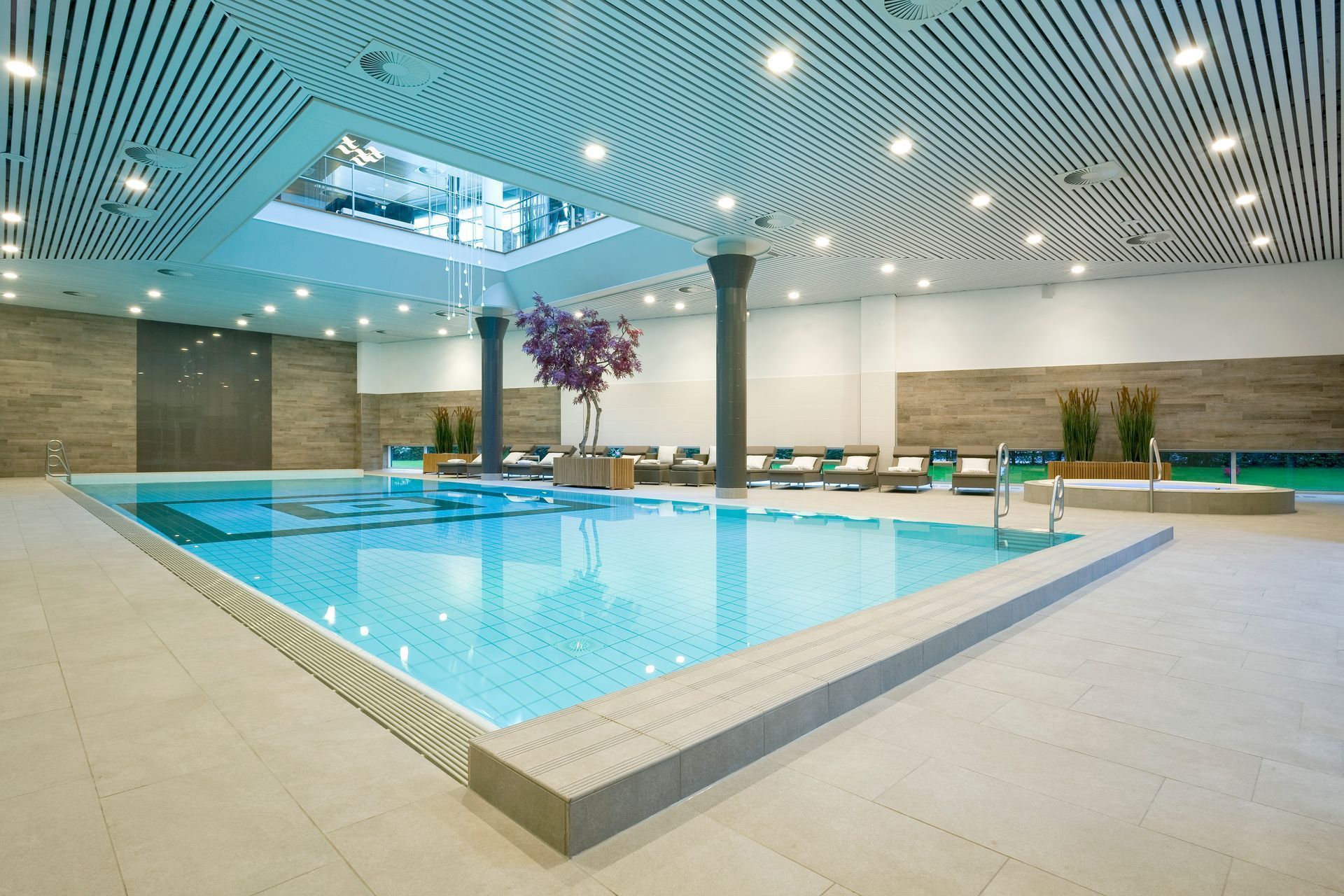 Indoor swimming pool with turquoise water, neutral tile, and a skylight.