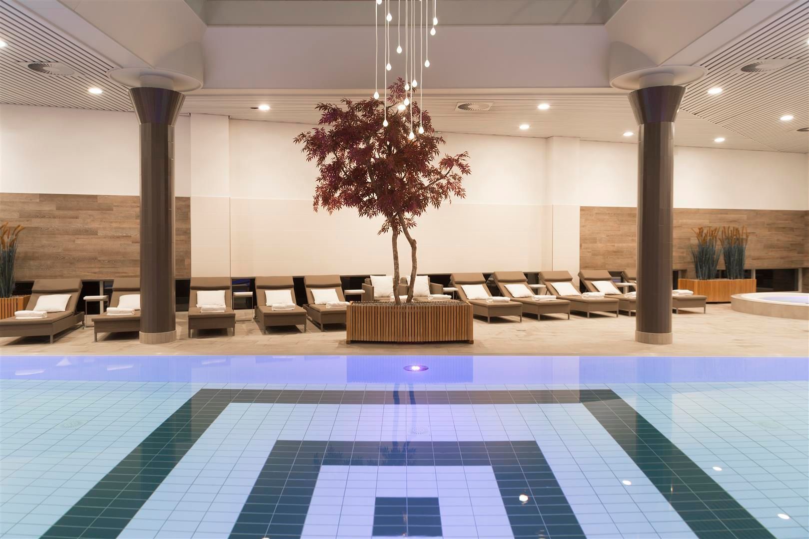 Indoor pool area with lounge chairs, columns, and a small tree.
