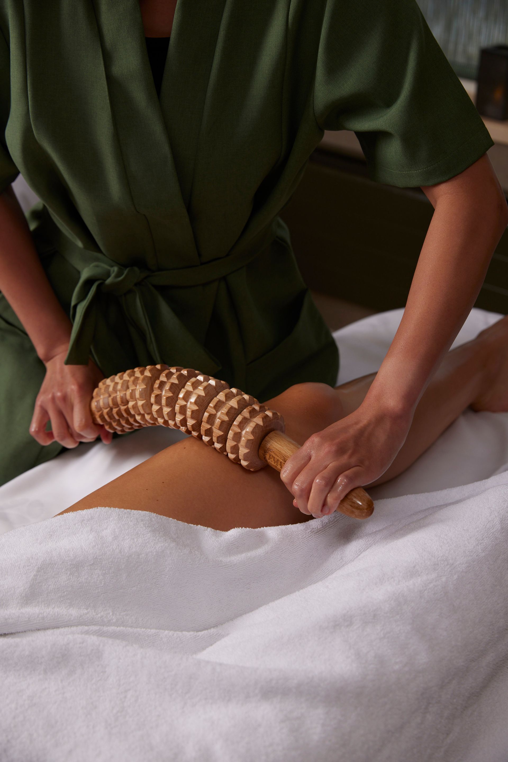 Therapist using a wooden roller on a client's leg during a spa treatment.