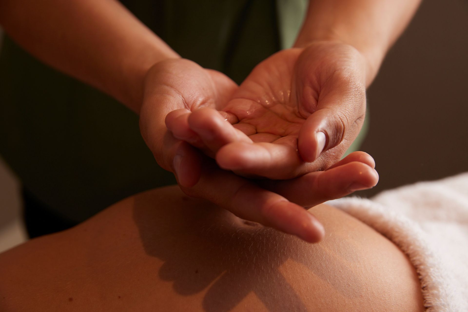 Hands, covered in oil, preparing to massage a person's back.