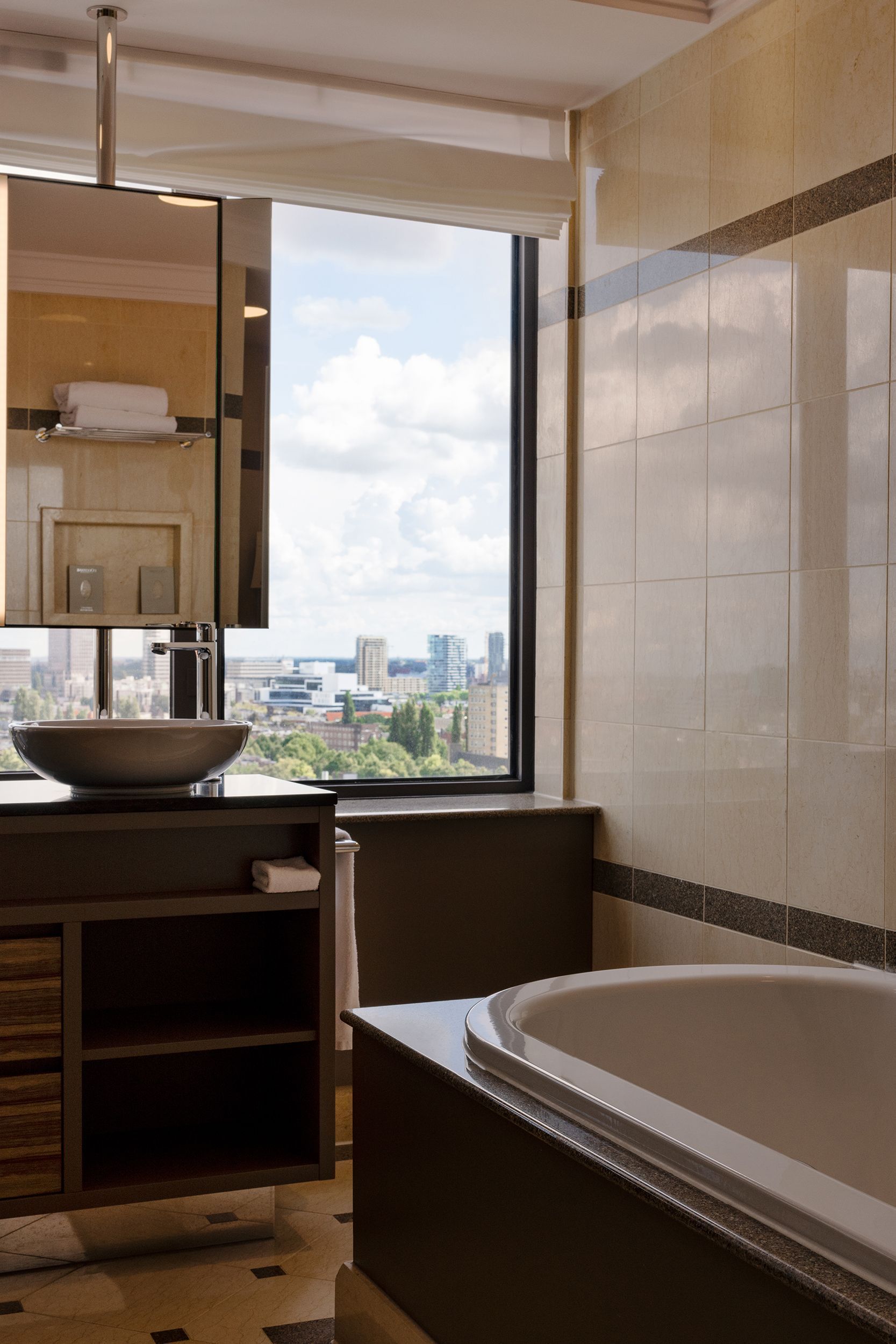 Bathroom with city view, featuring a tub, sink, vanity, mirror, and tiled walls.
