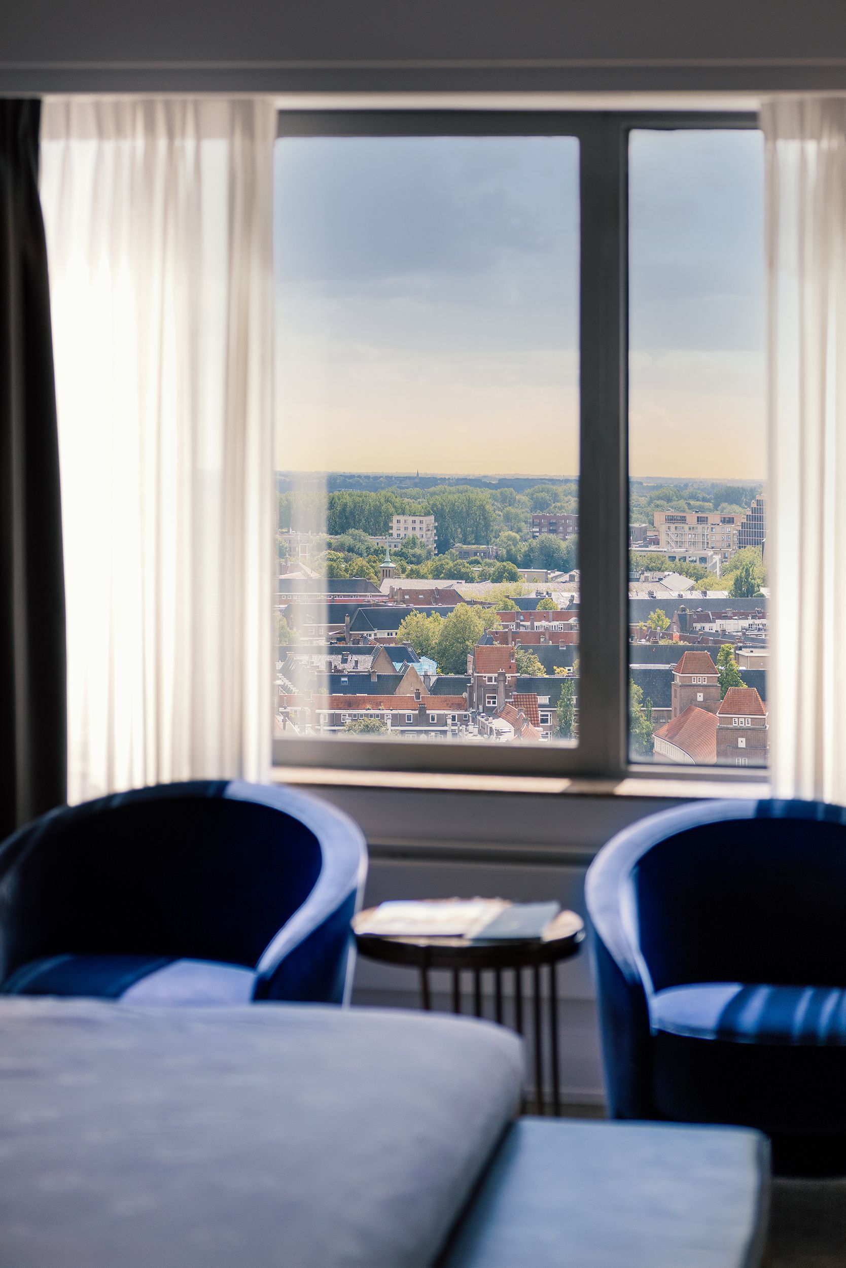 Blue chairs face a window with a city view, sheer curtains frame it.