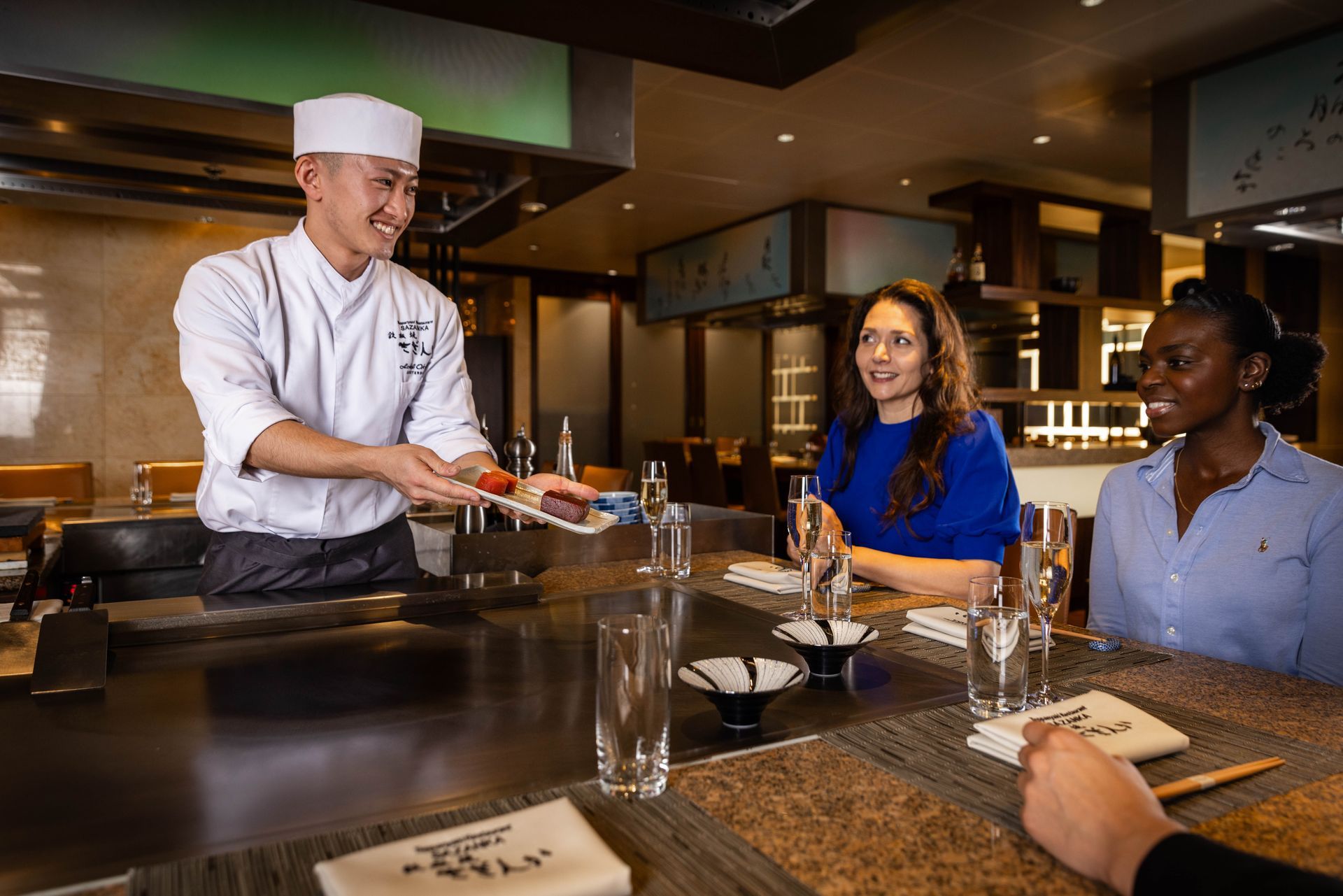 Chef serving food to two diners at a teppanyaki grill in a restaurant.