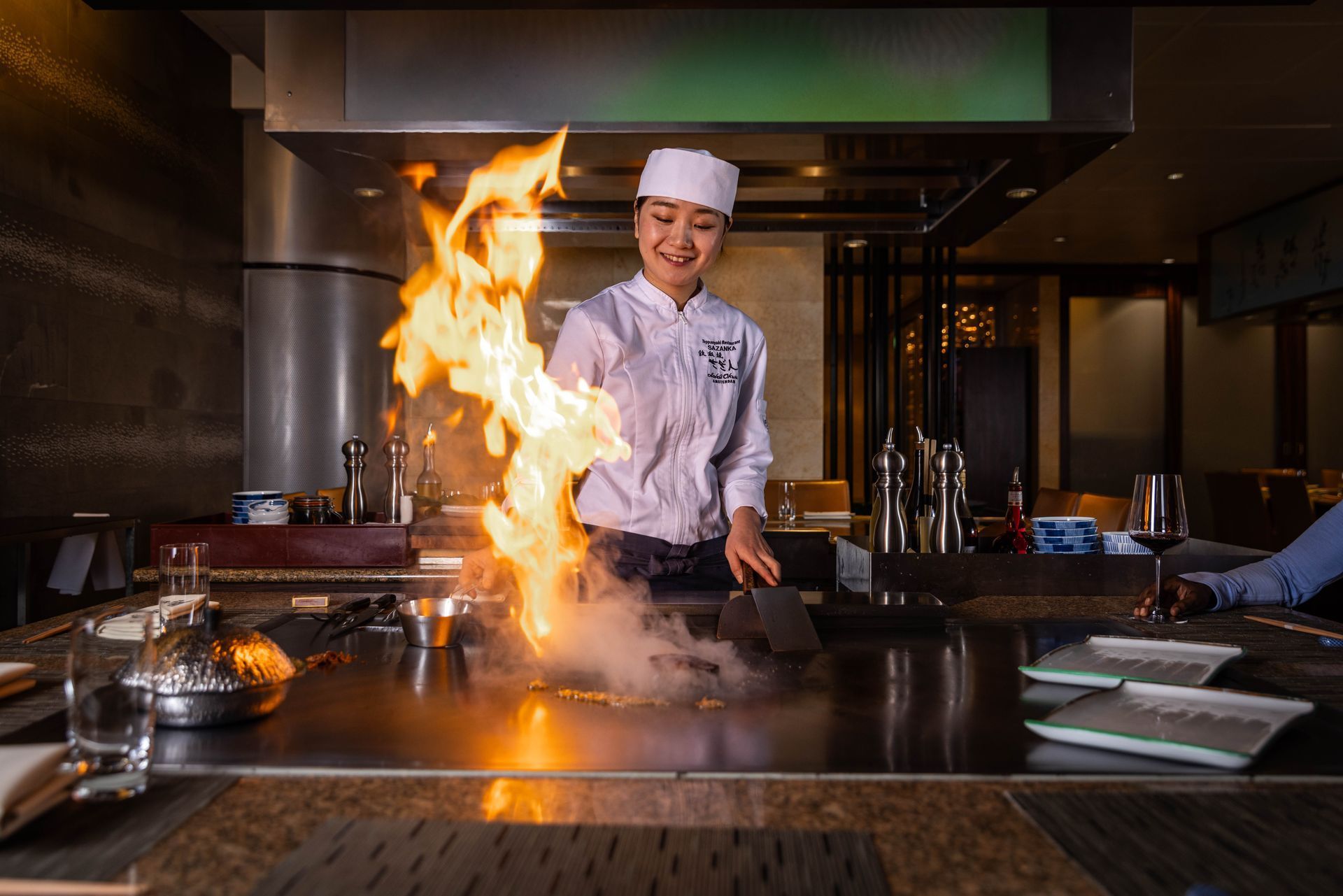 Chef ignites a large flame on a teppanyaki grill in a restaurant.