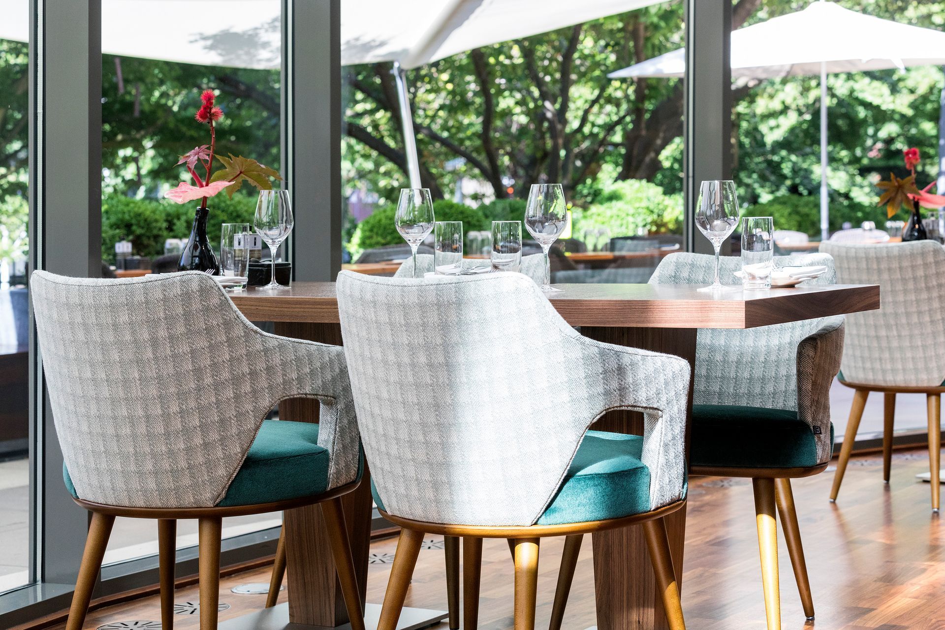 Restaurant table set for dining, with upholstered chairs, overlooking a lush garden.