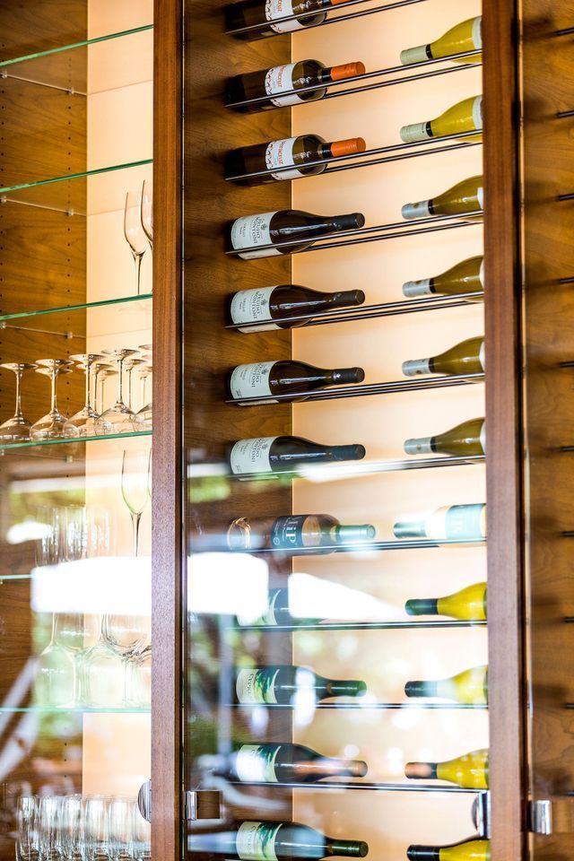 Wine bottles displayed in a wooden cabinet with glass shelves, visible through glass door.