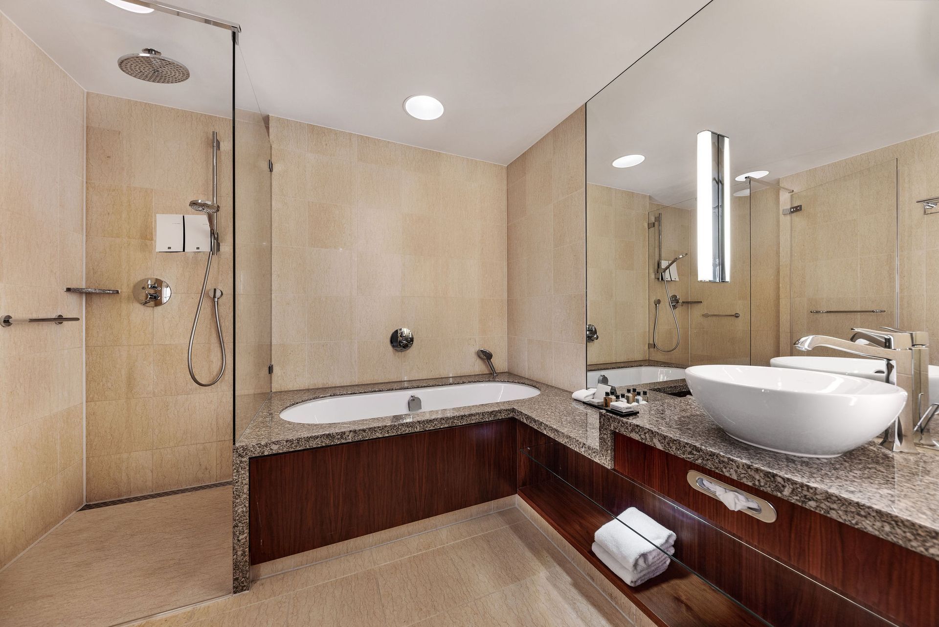 Modern bathroom with a shower, bathtub, and vanity with a sink. Beige walls and a dark wood cabinet.