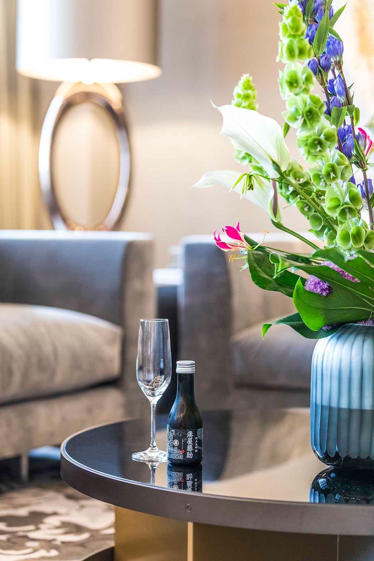 Round table with champagne glass, bottle, and vase of flowers in an elegant room.