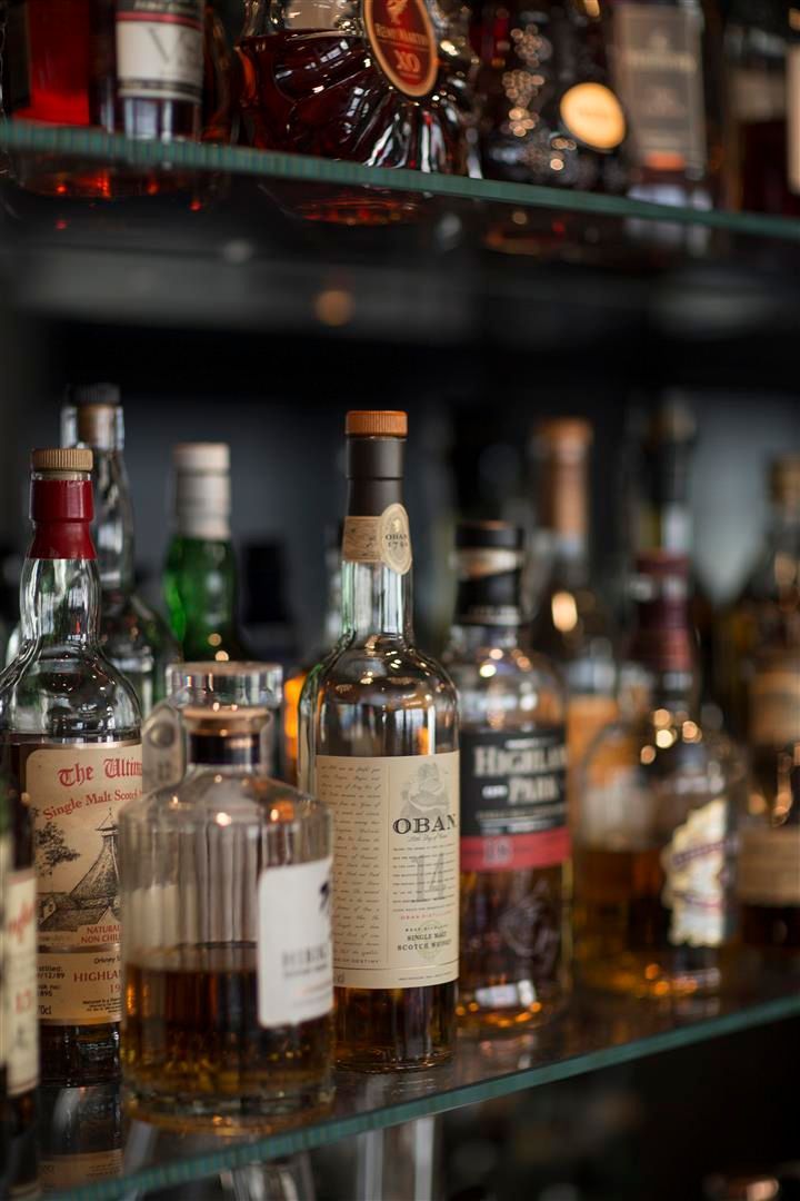 Bottles of liquor on glass shelves in a bar, various labels and colors, blurred background.