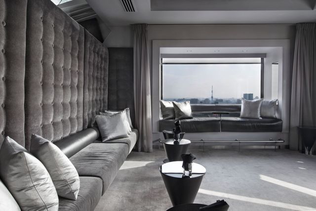 Gray modern interior with window seat overlooking a city; tufted wall, velvet sofa, silver pillows, and small tables.