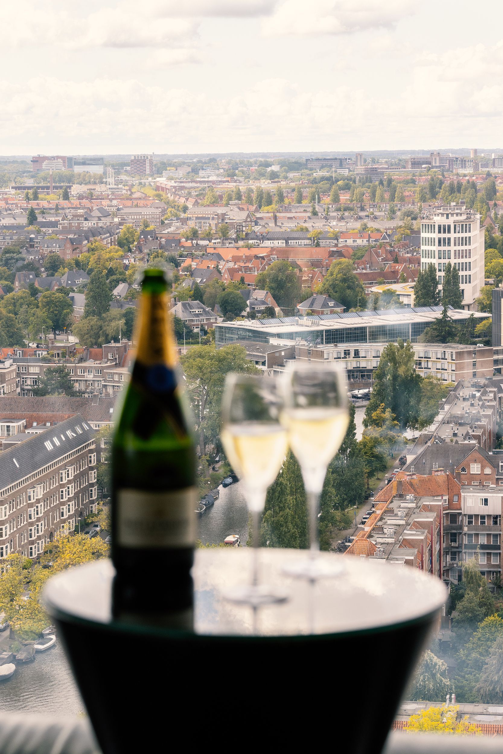 Champagne bottle and two glasses on table overlooking city.