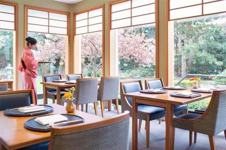 Restaurant interior with tables and chairs, large windows overlooking a garden, person in kimono.