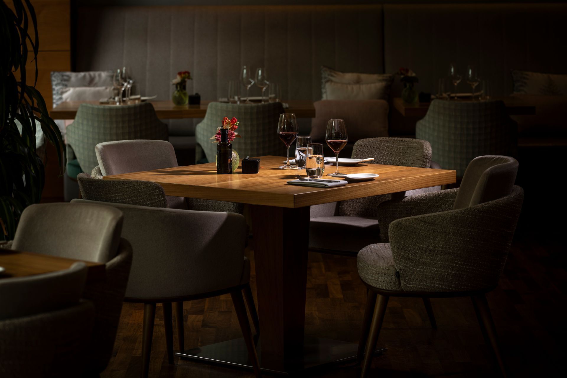 Restaurant table set for dining, surrounded by upholstered chairs. Low lighting, wooden table, wine glasses.